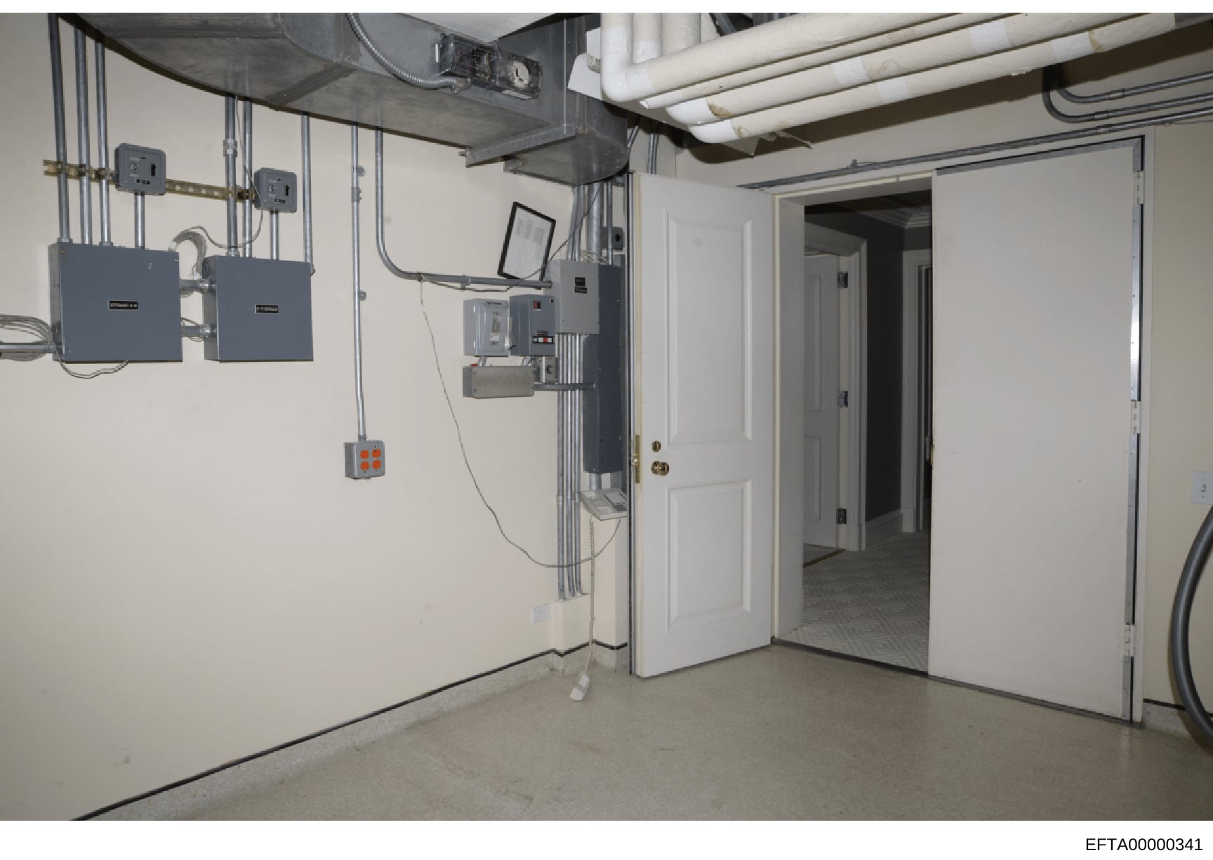 This is an evidence photograph showing the interior of a basement or utility room featuring electrical panels, wiring systems, and access doors. The image documents the infrastructure of what appears to be a property under investigation, with visible