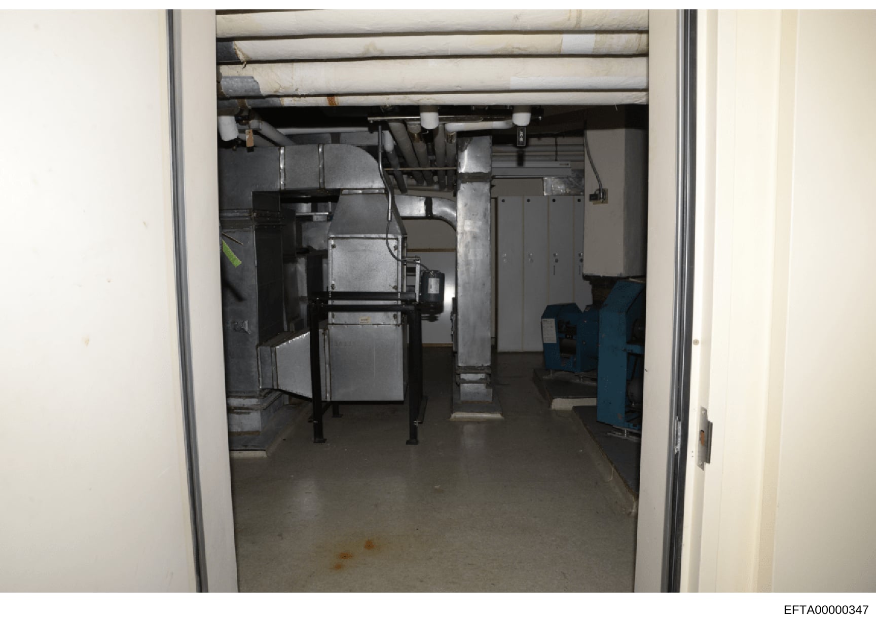 This photograph shows an interior mechanical or equipment room, likely in a basement or utility area of a building. The room contains industrial HVAC equipment, metal ductwork, electrical panels, and various mechanical systems. The image appears to b