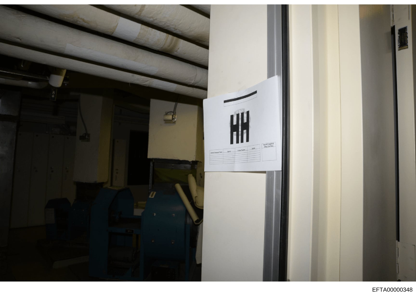 This photograph documents an interior space, likely a basement or utility room, with industrial piping overhead and evidence collection markers visible. A white sheet with tally marks (indicating a counting or tracking system) is affixed to the wall,