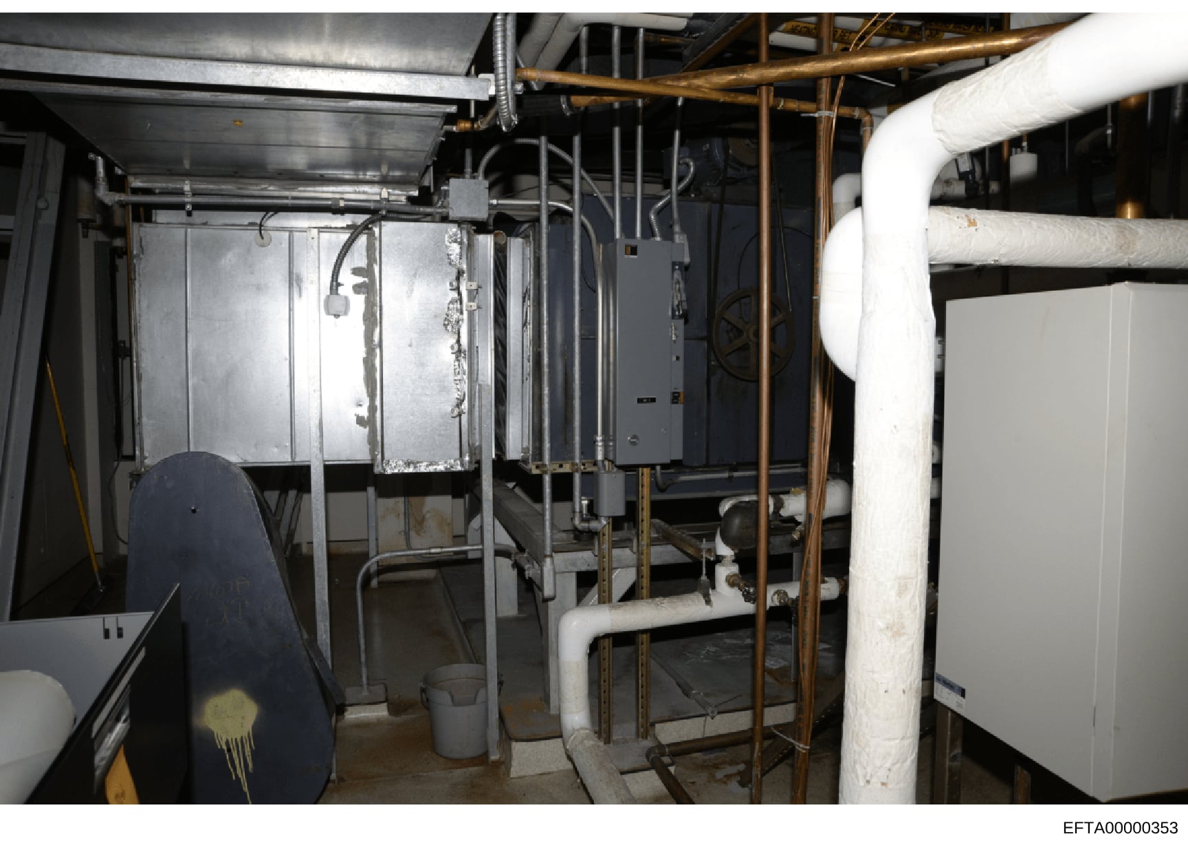 This is an evidence photograph showing the basement or utility area of a property, featuring HVAC equipment, piping systems, electrical components, and other mechanical installations. The image documents the infrastructure and layout of building syst