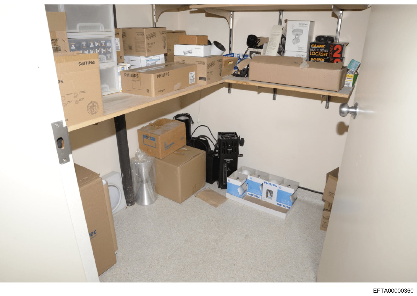 This photograph documents the contents of a storage room or closet space, showing shelving units filled with numerous cardboard boxes, electronic equipment, and miscellaneous items. The image appears to be evidence documentation from the investigatio