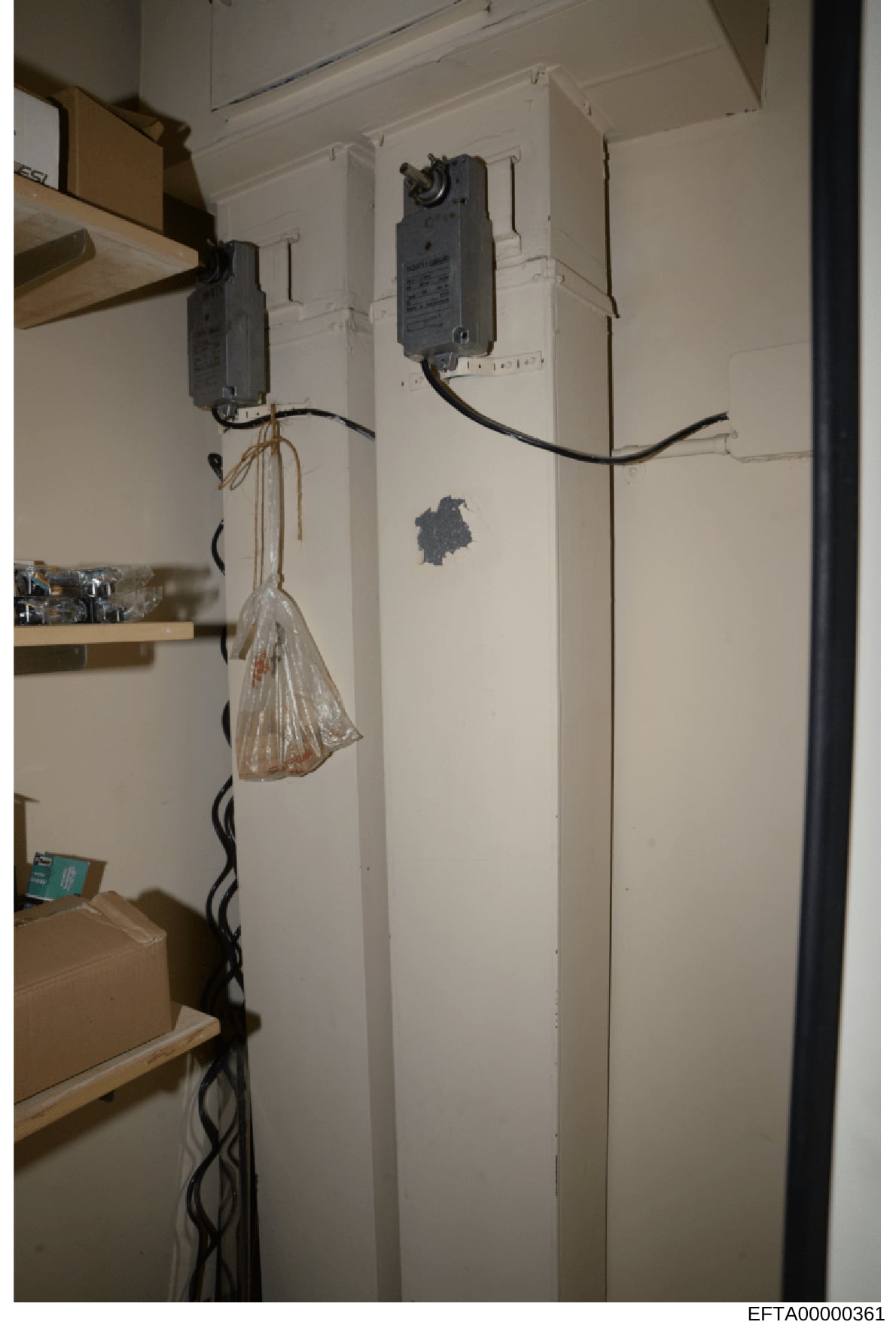 This is a photograph of an interior wall installation showing electrical wiring, two wall-mounted electrical boxes with switches/outlets, a coiled black power cord, and a clear plastic bag hanging from the left electrical box. The image appears to be