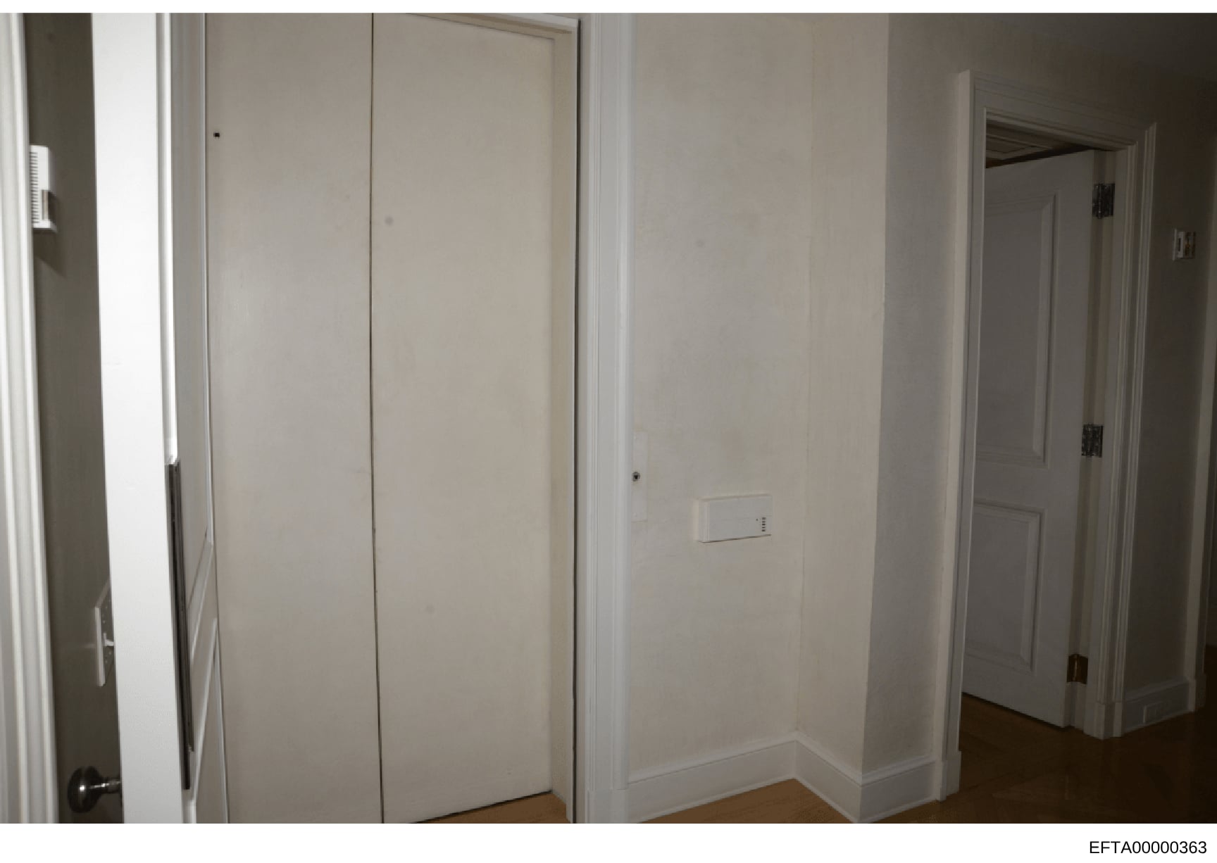 This is an evidence photograph showing the interior of a residential room with white walls, closet doors, and hardwood flooring. The image appears to be documentation of a property space, likely from the Jeffrey Epstein investigation. The room is spa