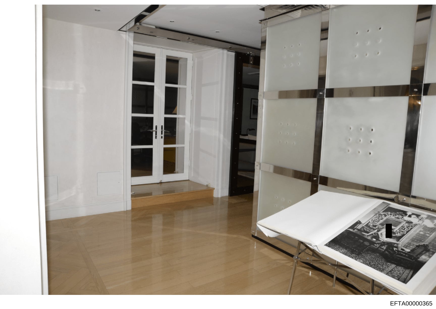 This is a photograph of a modern, minimalist interior space featuring white cabinetry, polished flooring, and what appears to be a walk-in closet or dressing area. A table in the foreground displays what appear to be architectural or design materials