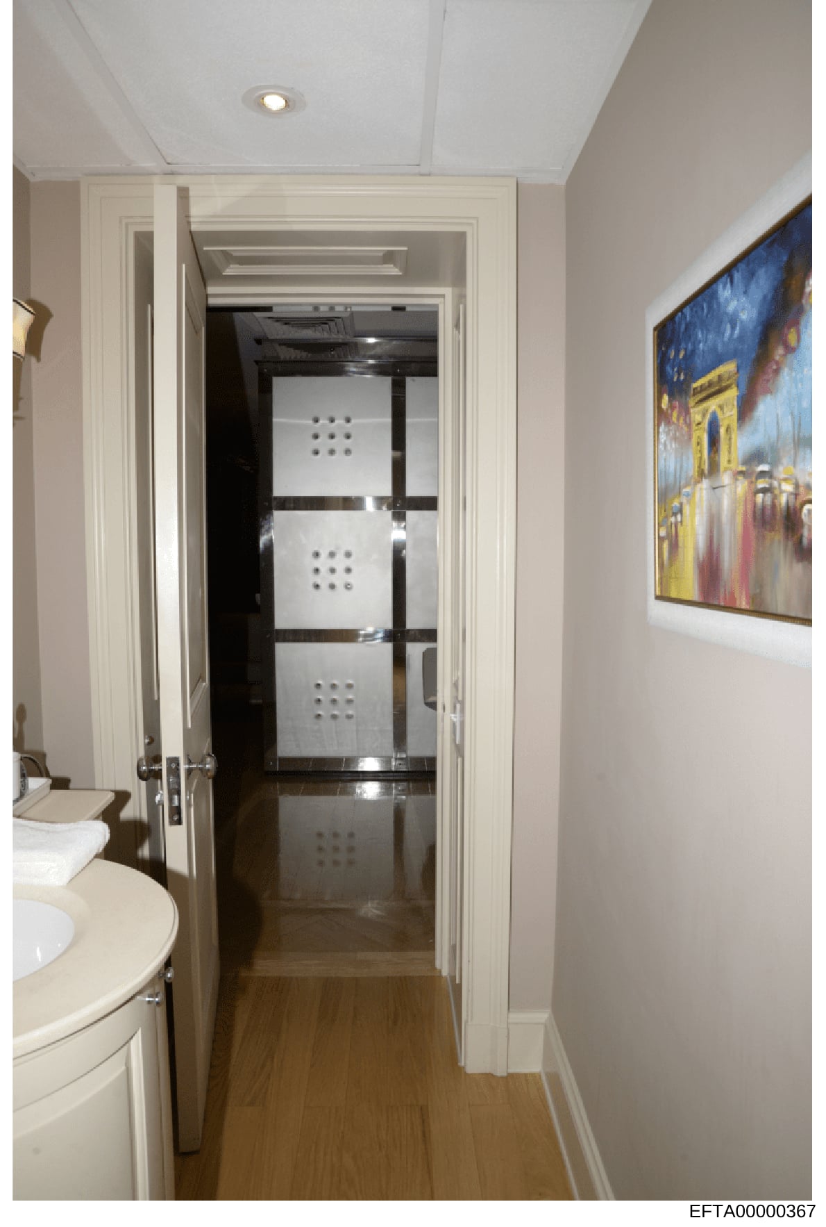 This is a photograph of an interior space showing a modern bathroom area with a cream-colored sink vanity on the left, white ceiling with recessed lighting, and a hallway leading to what appears to be a glass-partitioned room or closet with ventilati