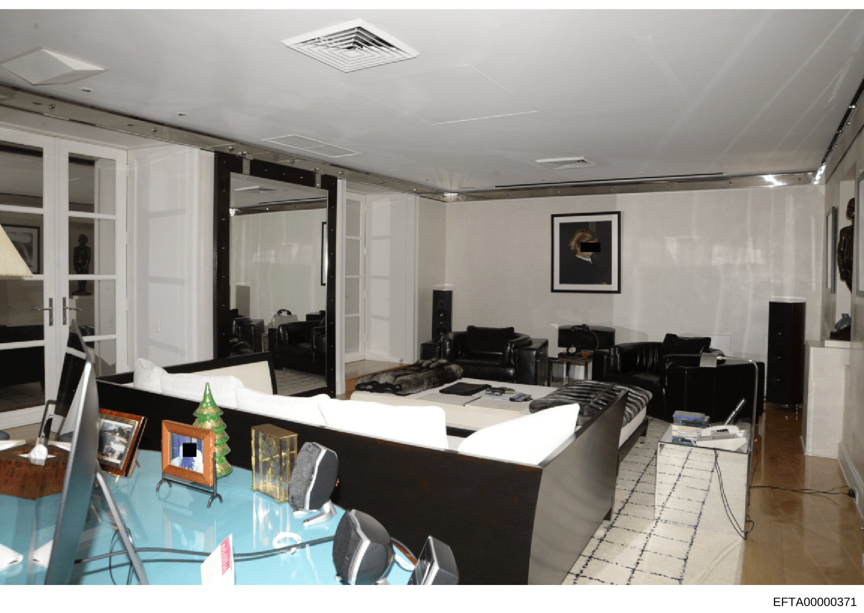 This is a photograph of an upscale interior room, featuring a modern aesthetic with white and black color scheme. The space contains contemporary furniture including leather seating, a large white counter or desk, mirrored elements, and decorative ar