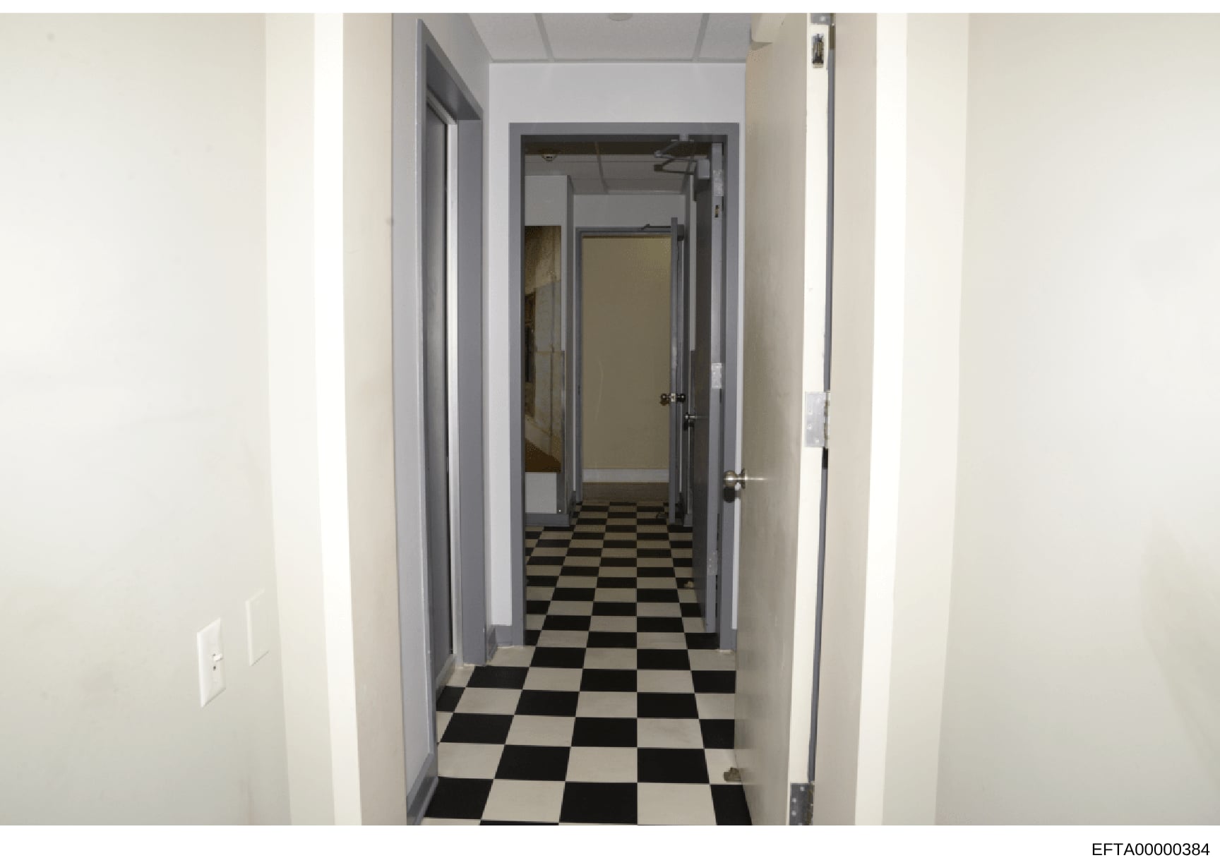 This is a photograph of an interior hallway, likely from one of Jeffrey Epstein's properties, showing a long corridor with black and white checkered tile flooring, white walls, and multiple doorways. The image appears to be part of the property docum