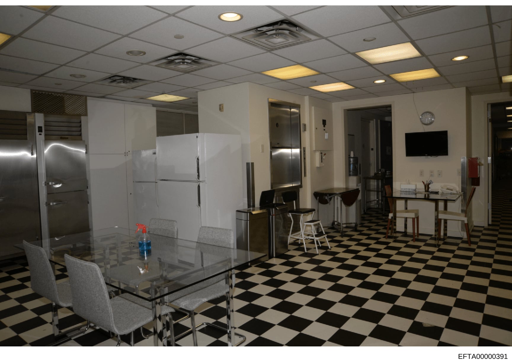 This is an evidence photograph showing the interior of what appears to be a commercial kitchen or employee break room with modern appliances, dining area, and institutional furnishings. The space features stainless steel refrigerators, white cabinetr