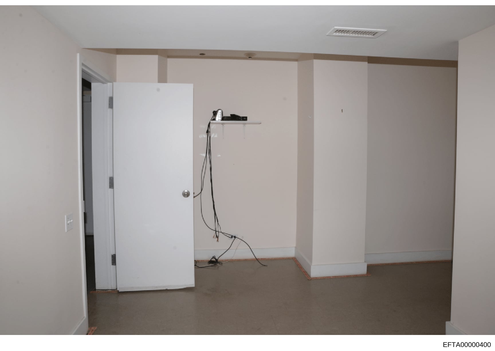 This is a photograph of an unfinished interior space showing white drywall partitions, exposed electrical wiring, and concrete flooring. The room appears to be in early-to-mid construction or renovation phase. The image was documented as evidence in