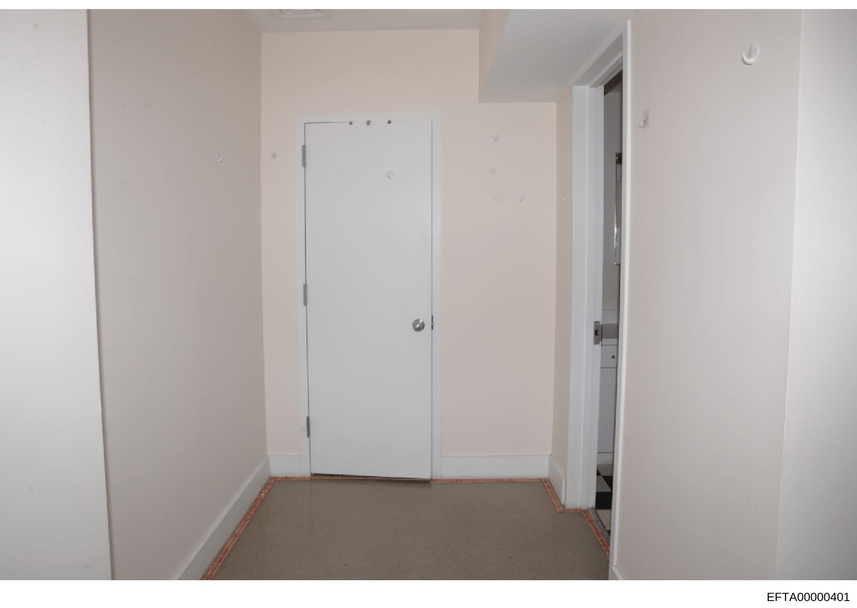This is an evidence photograph showing an interior room space, likely part of a property inspection or documentation. The room appears empty with white drywall, a white closet door in the center, and an open doorway to the right leading to another sp