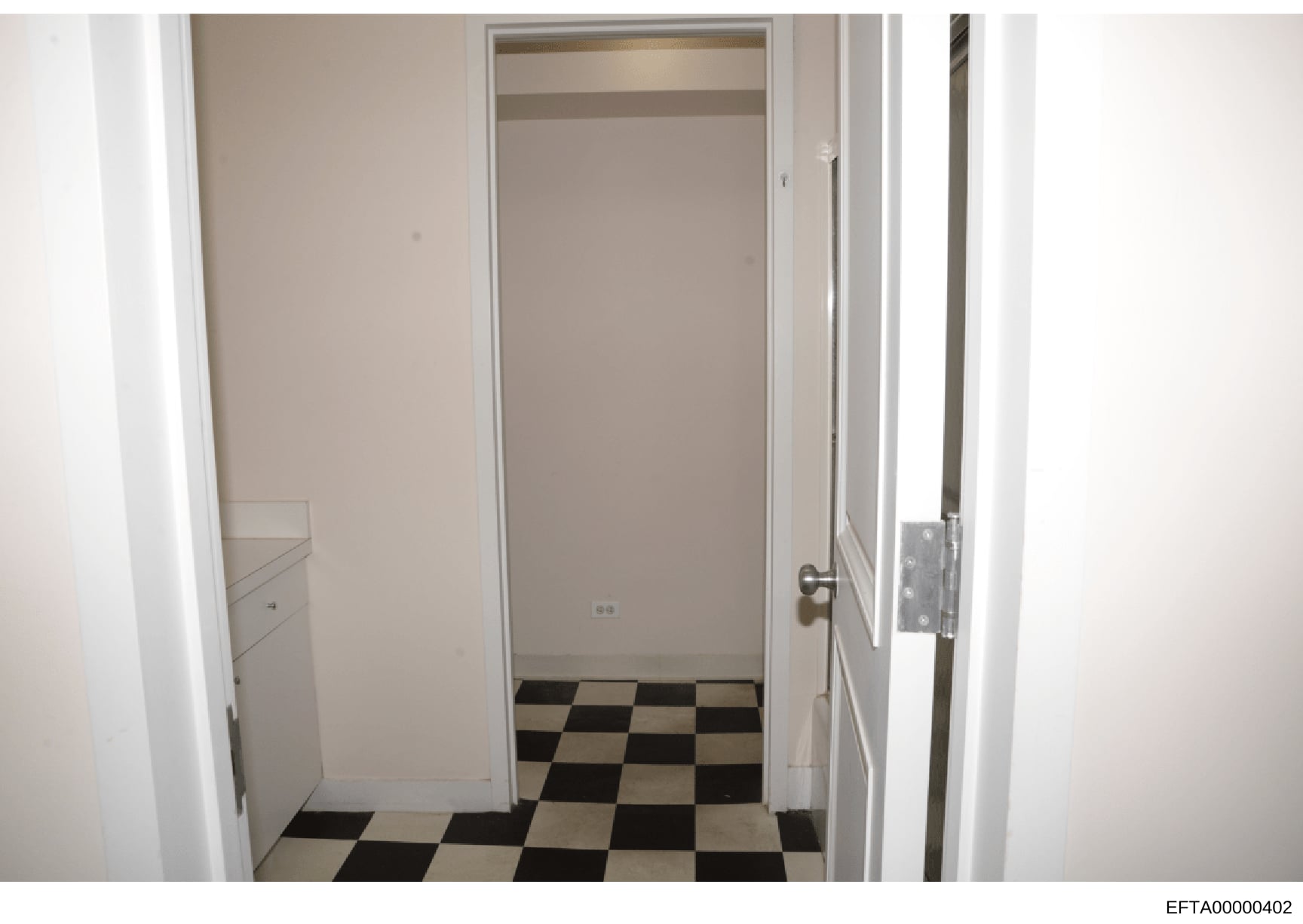 This is a photograph of an interior hallway or corridor featuring a distinctive black and white checkered floor pattern. The image shows white painted walls, framed doorways, and minimal furnishings. The photo appears to be documentation of a propert