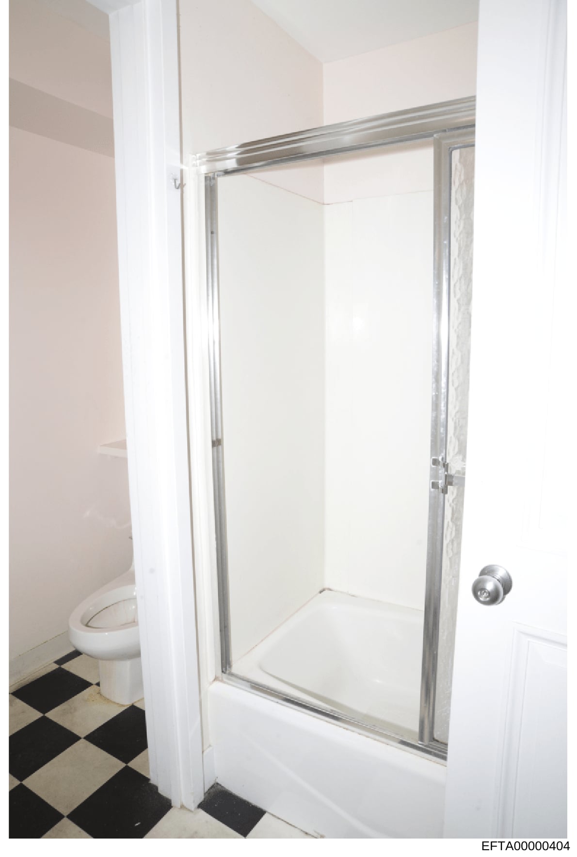 This is a photograph of a bathroom interior showing a shower stall with glass sliding doors, white tile walls, a white toilet, and a black-and-white checkered tile floor. The image appears to be documentation of property conditions, likely from one o