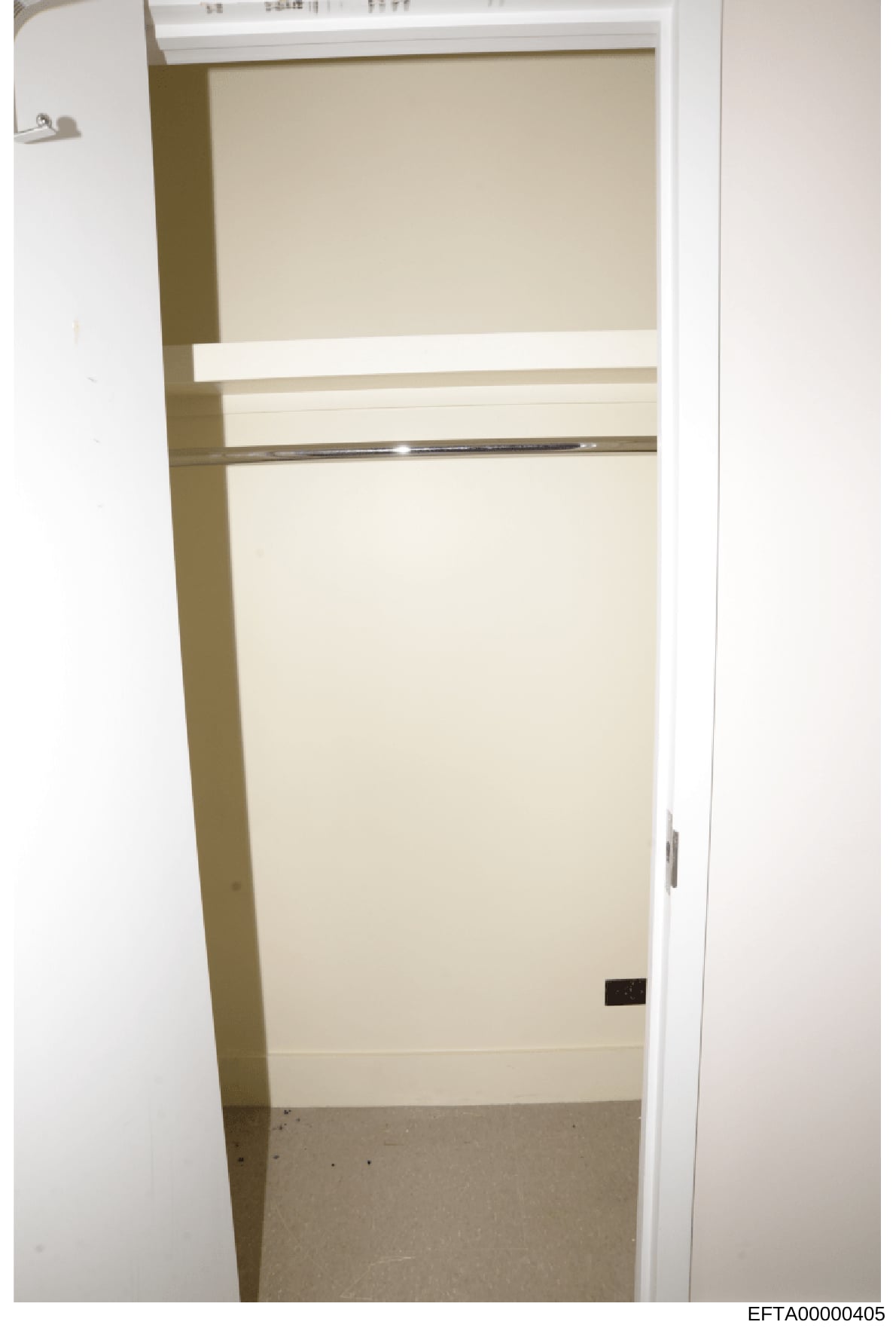This is a photograph of an empty interior room or closet space showing beige/cream-colored walls, white trim, and what appears to be a concrete or tiled floor. The image shows an open doorway with minimal furnishings or contents, possibly taken as ev
