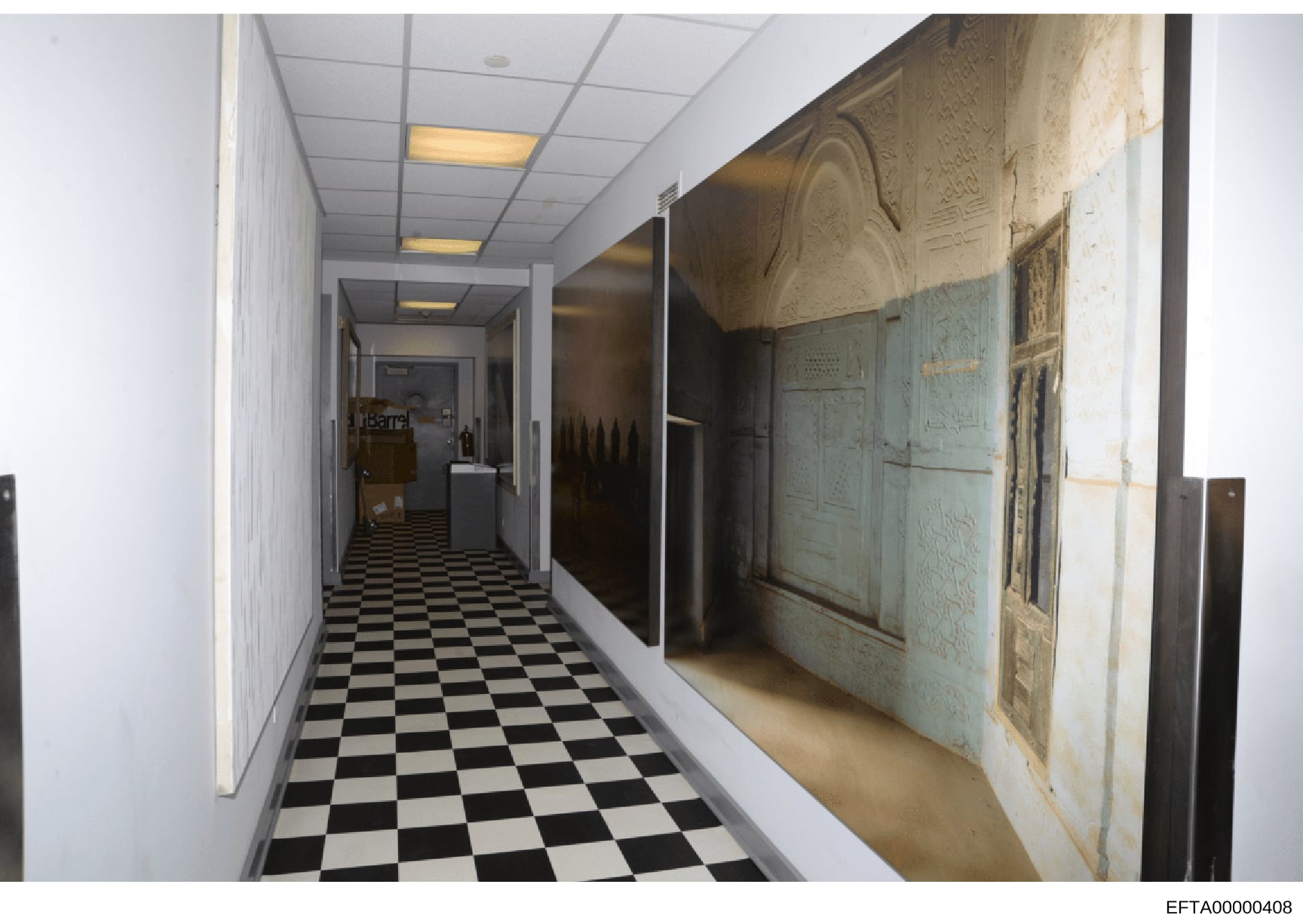 This photograph depicts a long interior hallway of what appears to be one of Epstein's properties, showing a distinctive black-and-white checkered floor, recessed ceiling lights, white walls, and ornate decorative panels or artwork on the right wall.