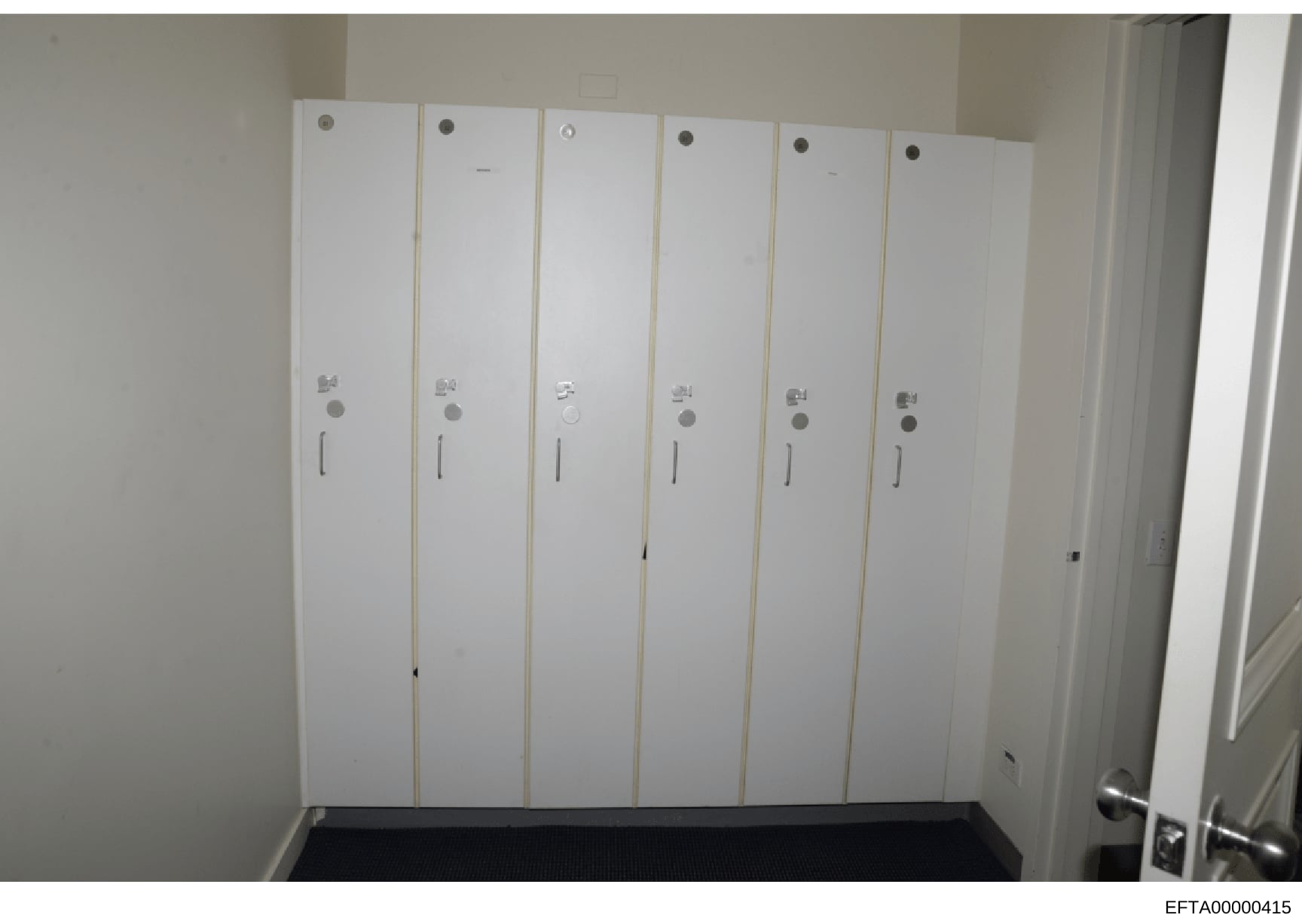 This photograph shows the interior of a room or closet containing six tall, white vertical cabinet or locker-style doors arranged side-by-side. Each door has similar hardware including a circular knob at the top and middle sections, with what appears