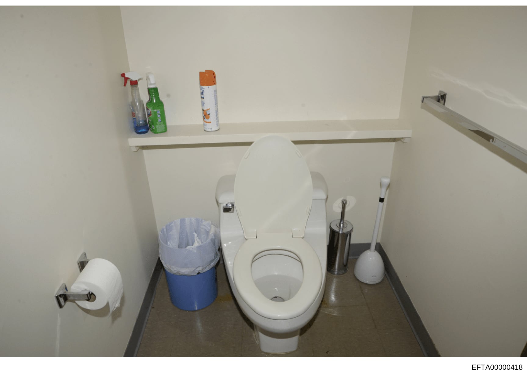 This is a photograph of a bathroom interior showing a white toilet, wall-mounted shelving with cleaning and personal care products, toilet paper holder, and waste bin. The image appears to be part of property documentation or evidence photography, wi