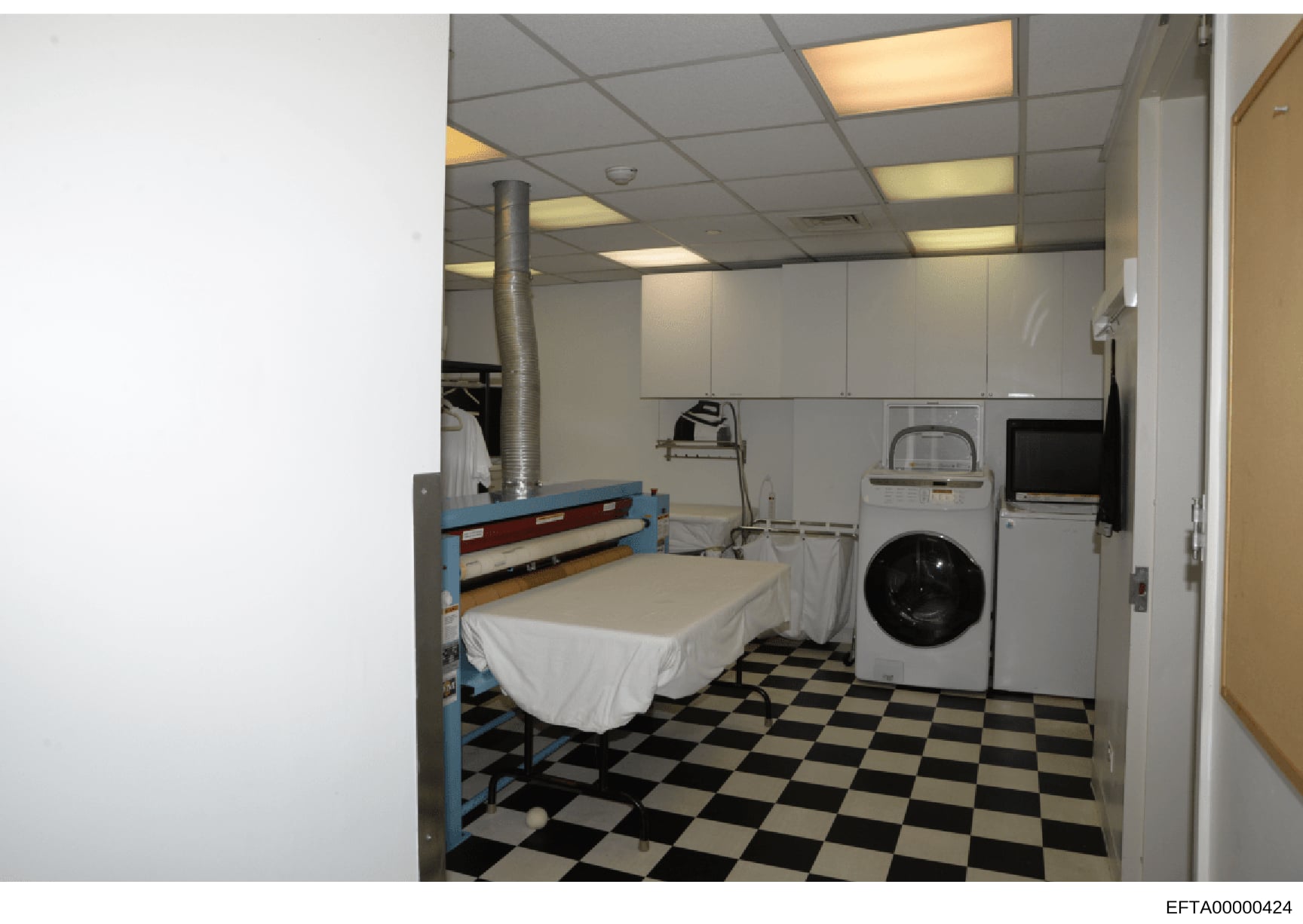 This photograph shows a combined bedroom and laundry area, likely part of staff quarters in one of Epstein's properties. The room contains a single bed with white linens, washing machine, dryer, and various household appliances. The space appears to