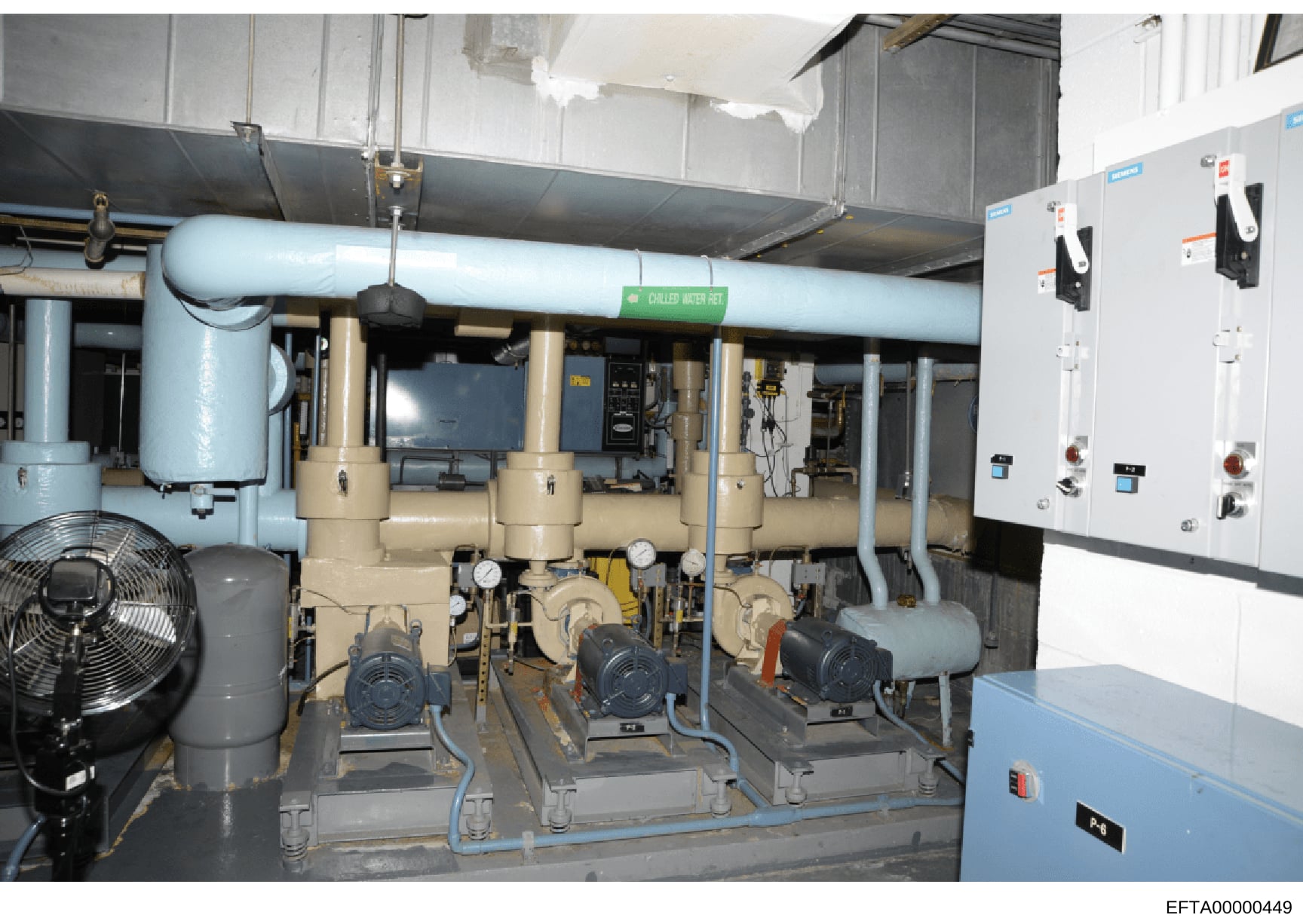This photograph shows the interior of a building's mechanical systems room containing industrial HVAC equipment, chilled water systems, pumps, compressors, and electrical control panels. The image documents the mechanical infrastructure of a property