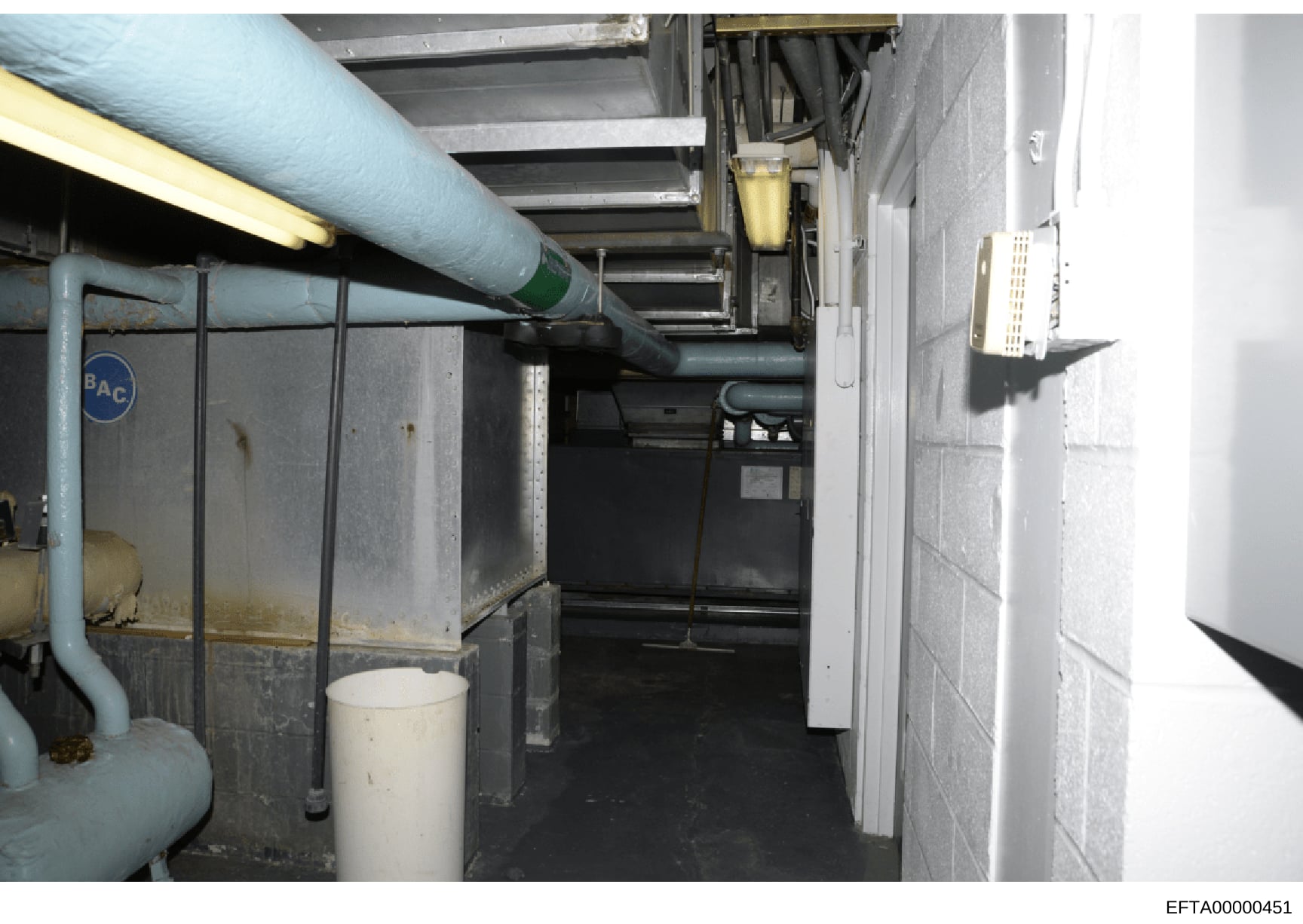 This is an evidence photograph showing an interior basement or mechanical space containing HVAC piping, ductwork, electrical systems, and various mechanical equipment. The image appears to be part of a property inspection or forensic documentation, w