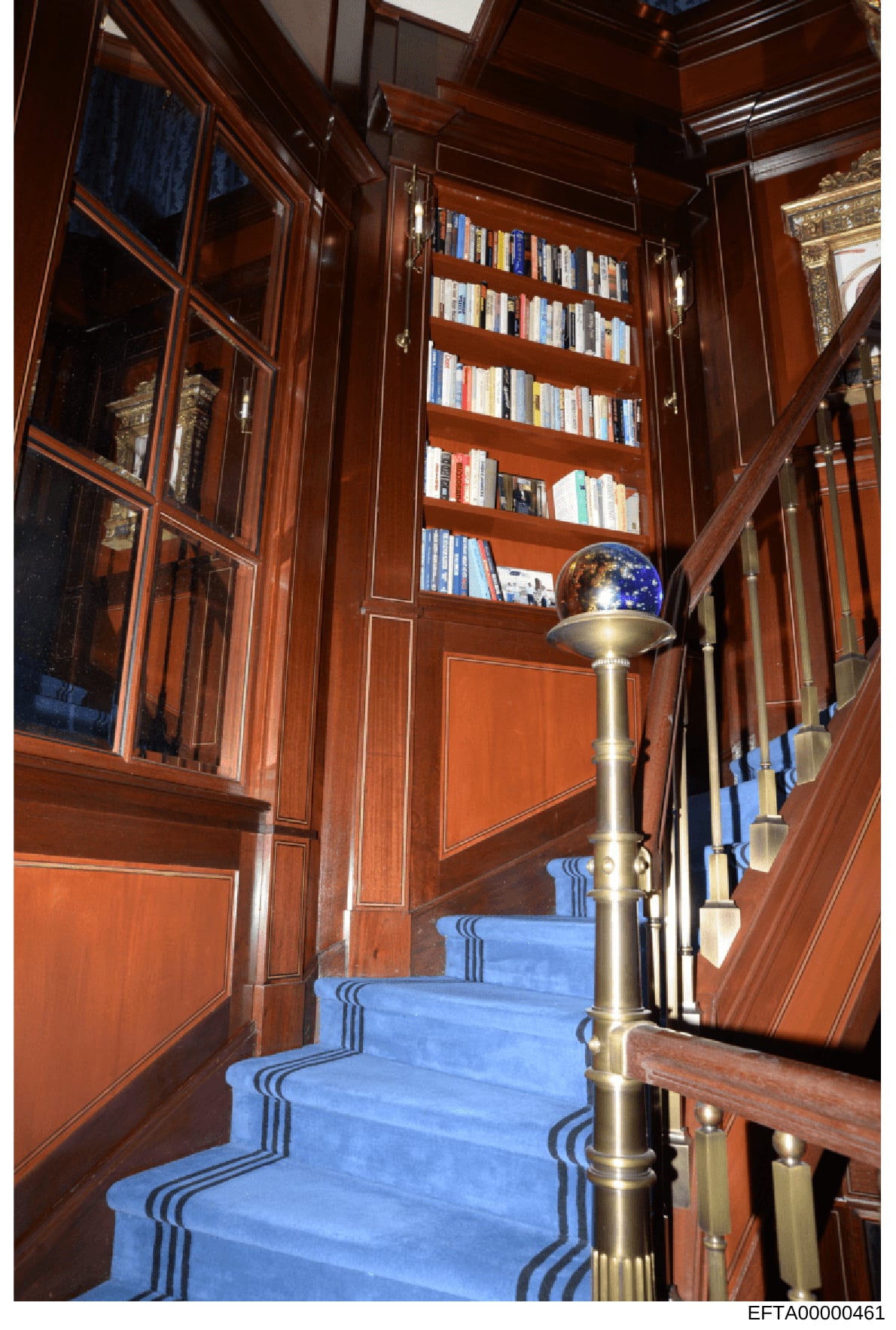 This photograph shows an elegant interior staircase with extensive built-in wooden bookshelves, decorative globe ornament, and luxurious finishes including blue carpeting with striped detailing. The image documents the interior design and décor of wh