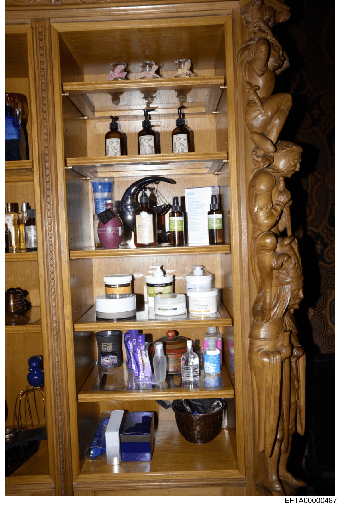 This photograph shows the contents of a wooden cabinet with glass doors containing various personal care items, cosmetics, fragrances, and grooming products. The image appears to be evidence documentation from a property search or inventory, showing 
