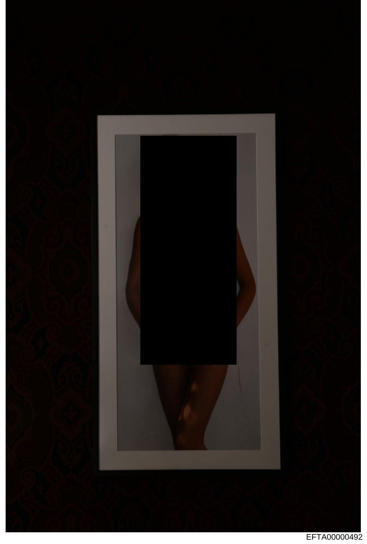 This is an evidence photograph showing a portrait of an individual with their face redacted or obscured. The photo appears to be a full-body or partial-body image taken against a neutral background, typical of investigative documentation. The large b