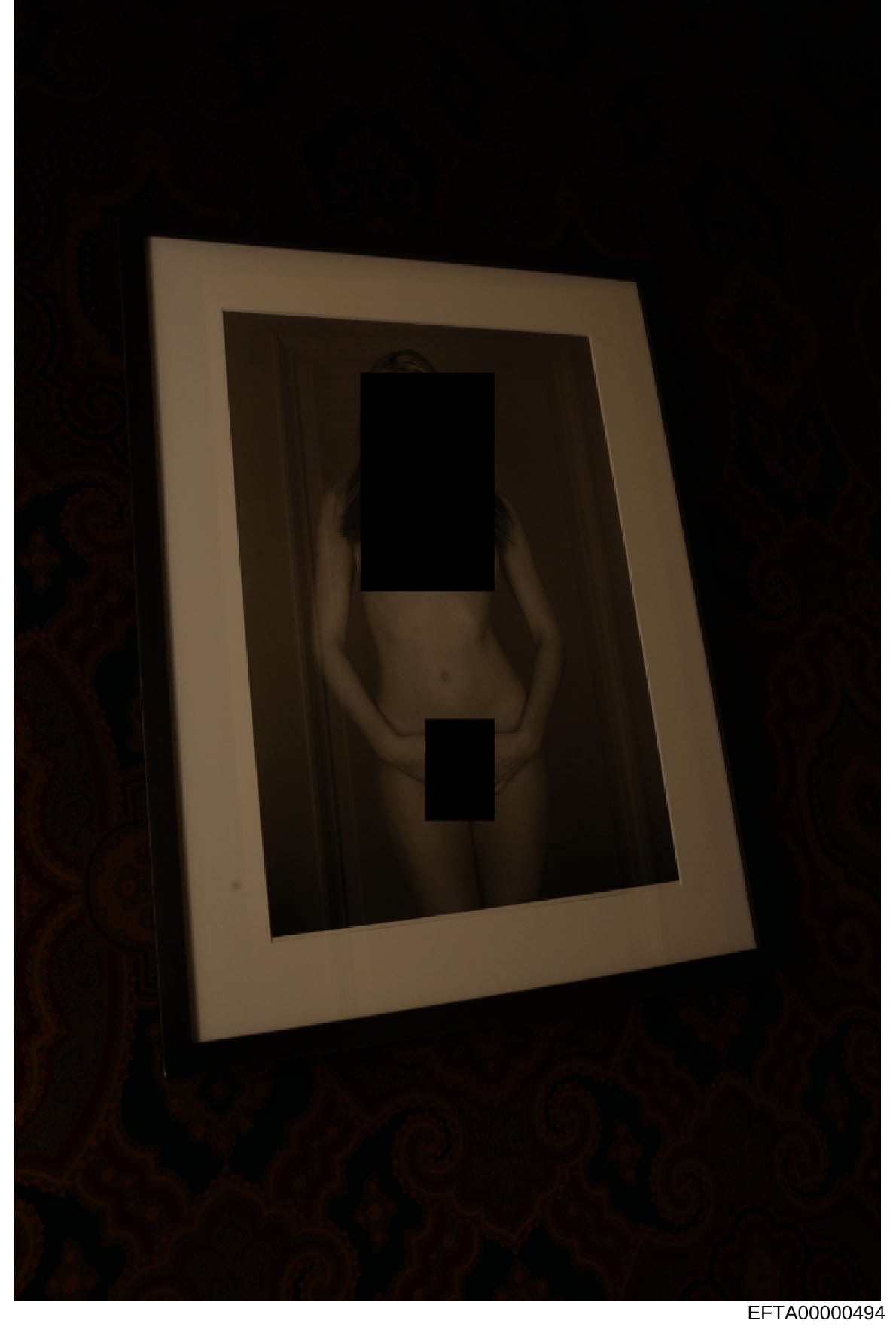 This is an evidence photograph showing a framed portrait with the subject's face and lower body pixelated/redacted for privacy protection. The image appears to be taken in low lighting conditions and shows the frame mounted or displayed against a dar