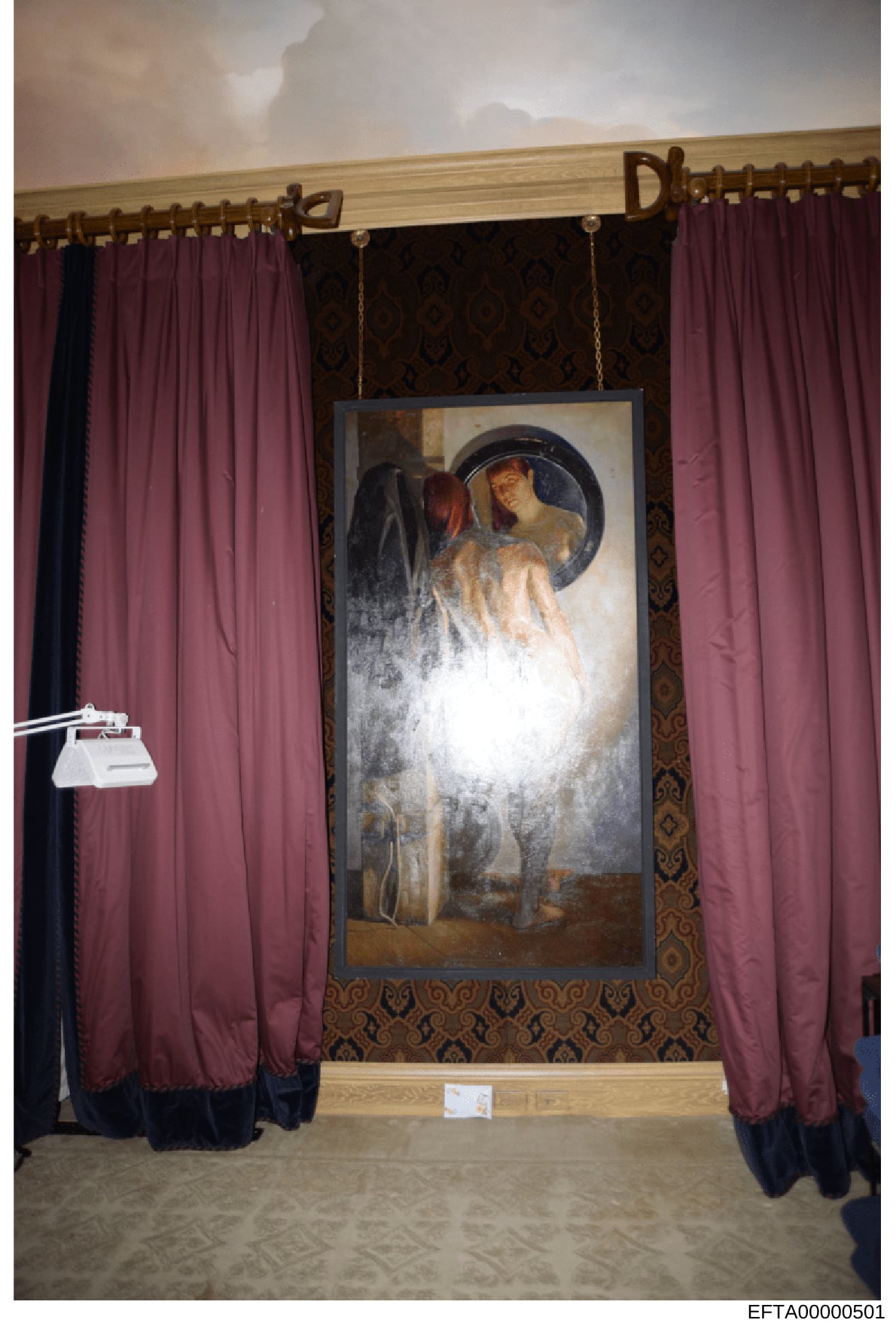 Photograph documenting an interior space, likely from one of Jeffrey Epstein's properties, showing a framed classical artwork depicting figures with a mirror or reflective element, flanked by burgundy and black curtains. The ornate wallpaper and wood