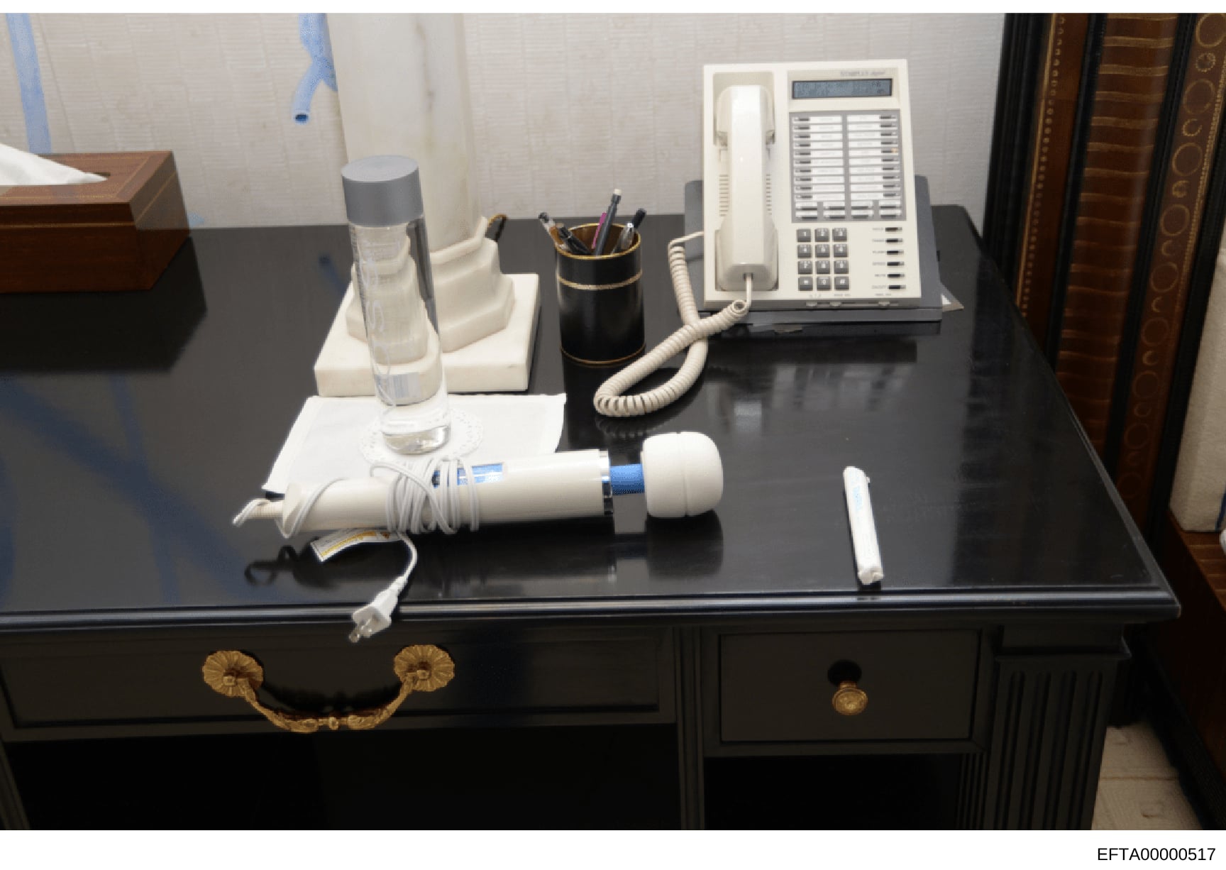Evidence photograph documenting a desk setup within an Epstein property, showing office furnishings and equipment including a multi-line telephone system, water glass, pen holder, and other desk accessories. This appears to be documentation of interi