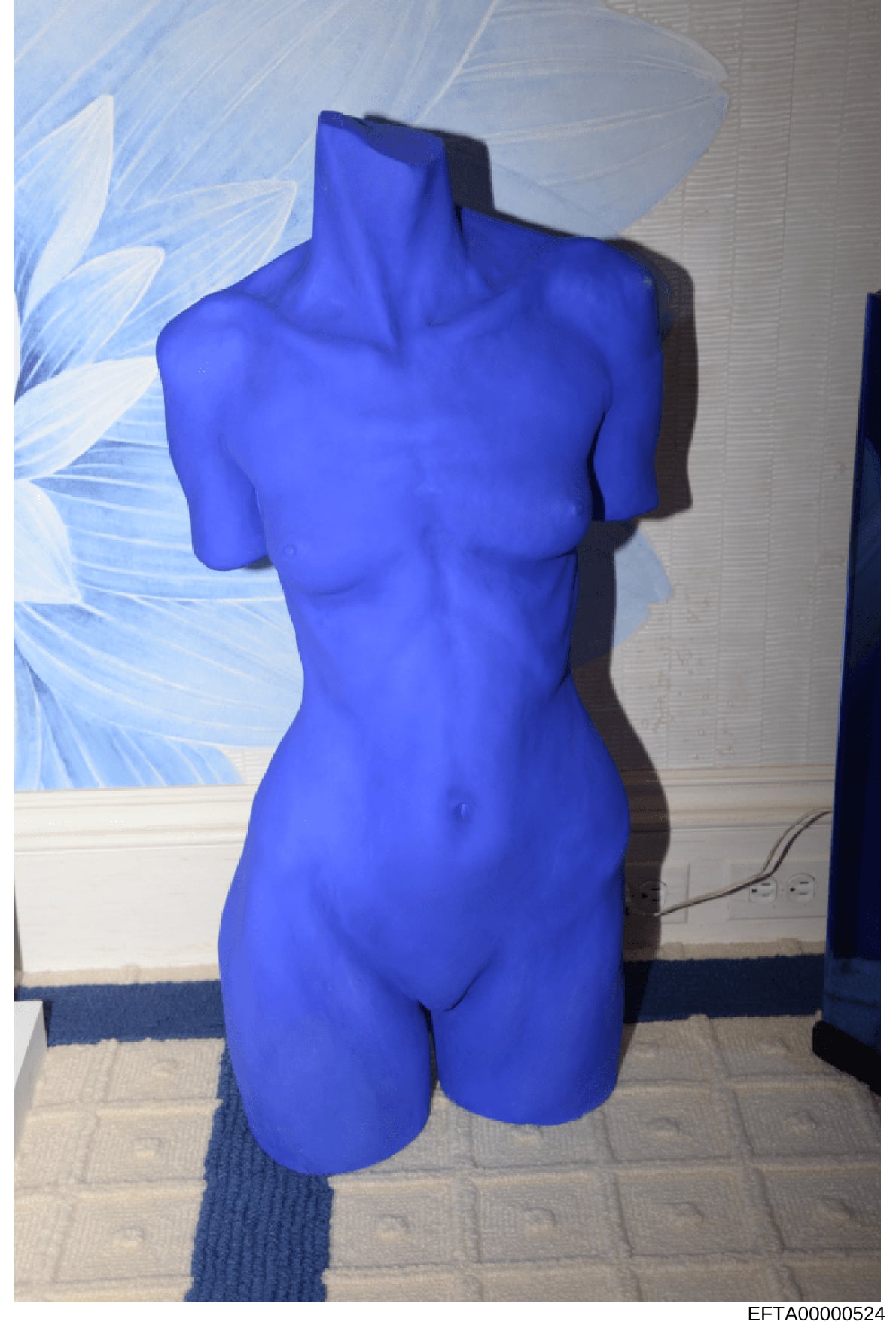 This is a photograph of a blue torso sculpture or art piece displayed indoors. The piece appears to be a headless, armless female form rendered in bright cobalt blue, positioned in what looks like an office or gallery space. The significance in the i