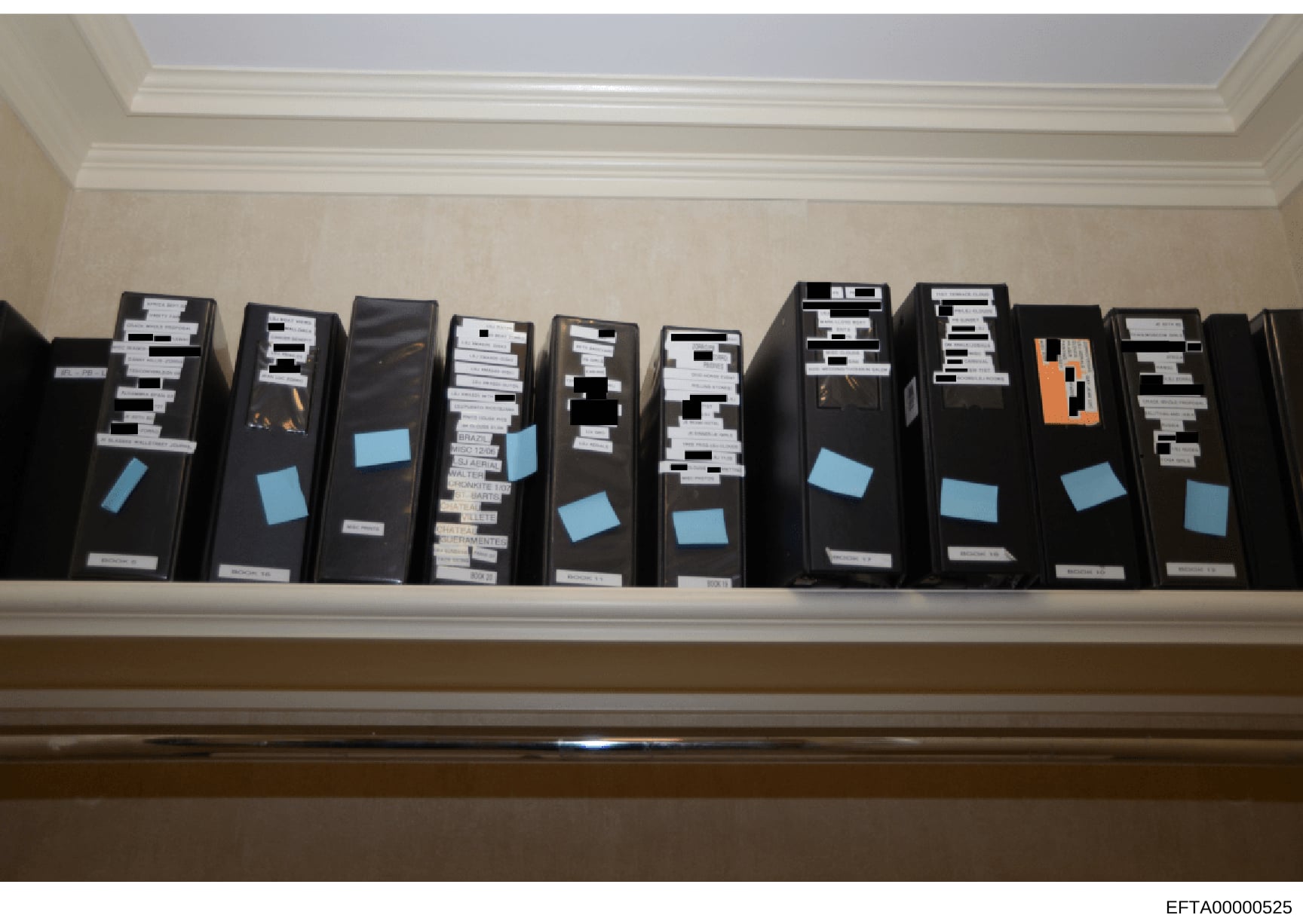 This photograph documents a shelf displaying approximately 10-11 black archival storage boxes containing investigation case files, evidence, and documents related to the Epstein case. The boxes are labeled with evidence tags and blue index stickers i