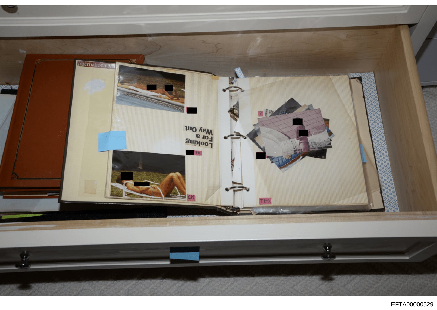 This is a photograph of a three-ring binder containing a collection of photographs and images, many of which have been redacted with black boxes by investigators. The binder appears to have been seized as evidence and is shown on a shelf in what appe