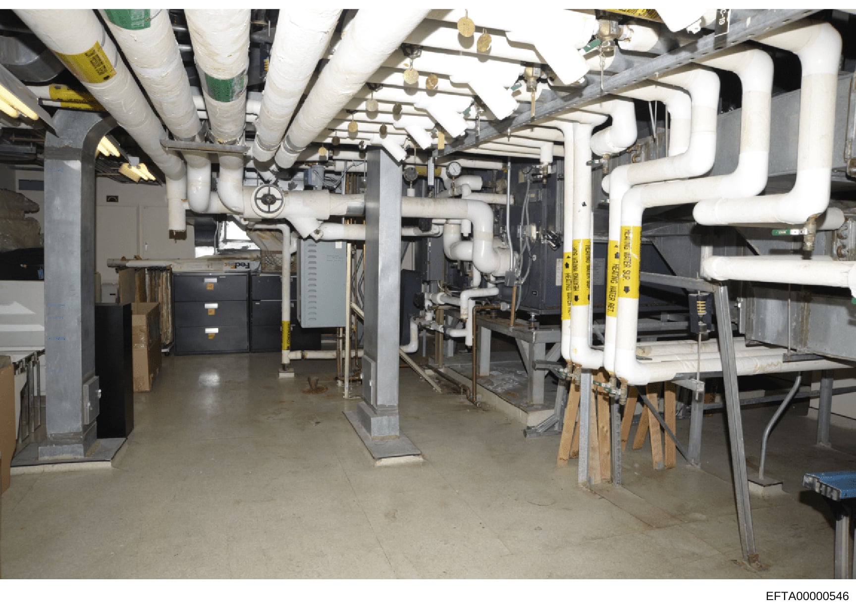 This photograph documents a basement or utility room showing extensive HVAC ductwork, plumbing systems, and mechanical equipment. The image appears to be an interior inspection or documentation photo of building infrastructure, likely from one of Eps