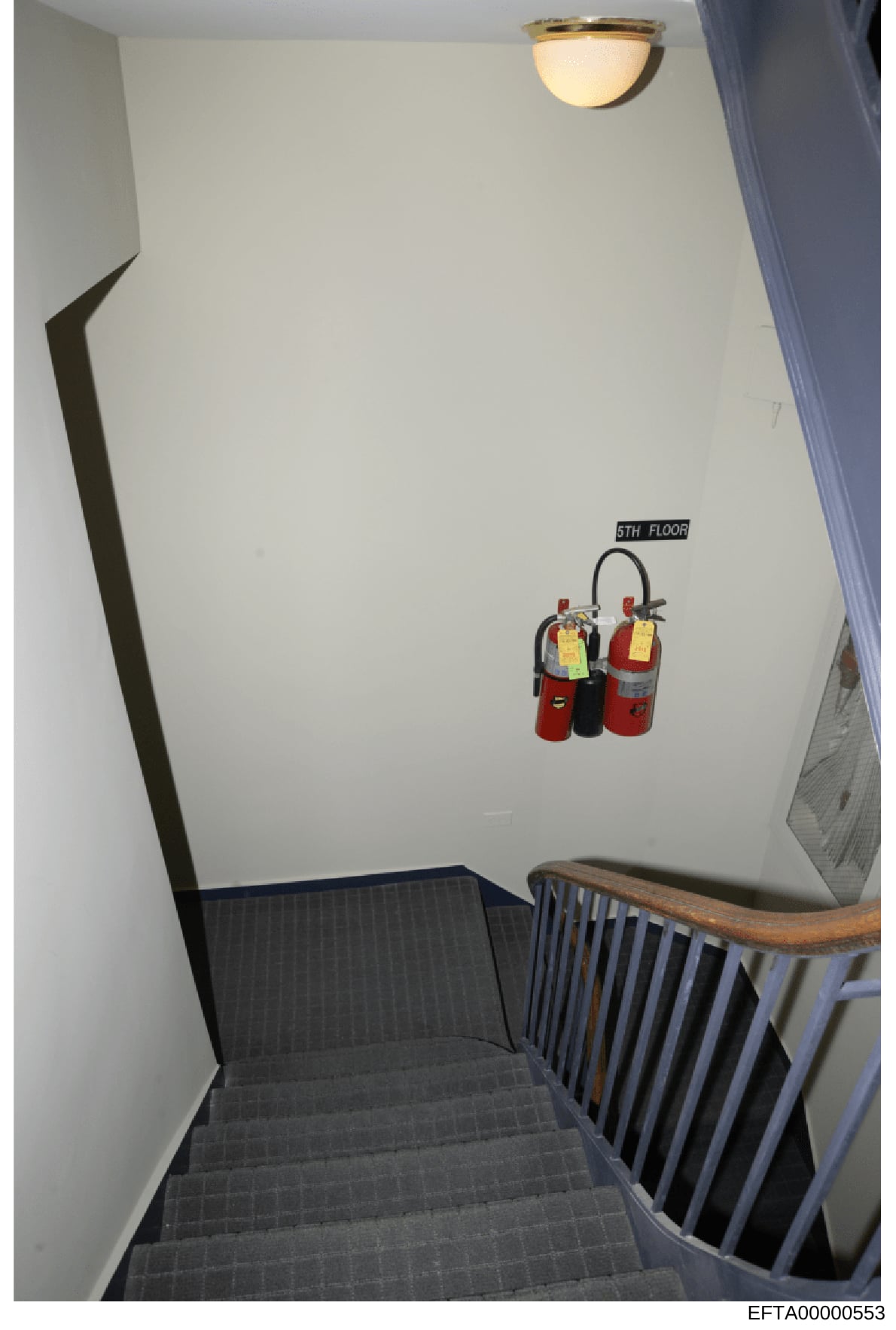 This is an evidence photograph of a stairwell interior on the fifth floor of a building, showing fire extinguishers mounted on the wall with inspection tags. The image documents building safety infrastructure and appears to be part of a property inve