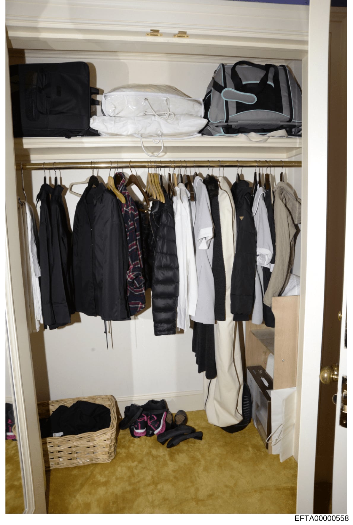 This is an evidence photograph showing the interior of a residential closet containing various clothing items, luggage, and personal belongings. The closet displays an organized collection of garments on hangers along with packed suitcases and storag
