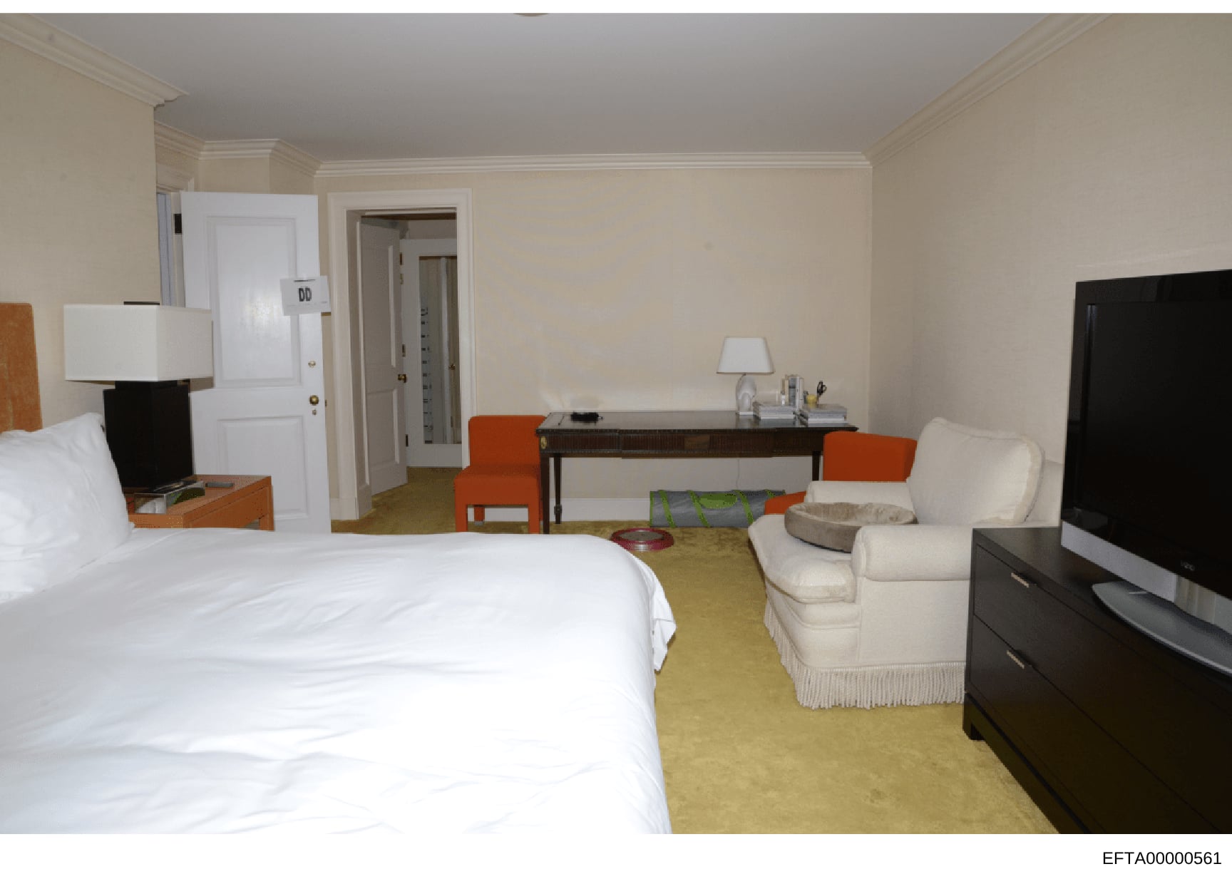 This photograph shows a hotel suite interior featuring a bedroom with a queen-sized bed, a living area with upholstered seating, and a work desk. The image appears to be documentation of accommodations, possibly related to properties or residences un