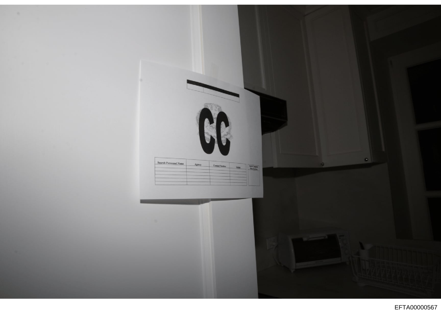This is an evidence photograph taken during the investigation showing an interior doorway or wall area marked with a large 'GG' reference label and an accompanying search log sheet. The marker and documentation sheet are standard forensic photography