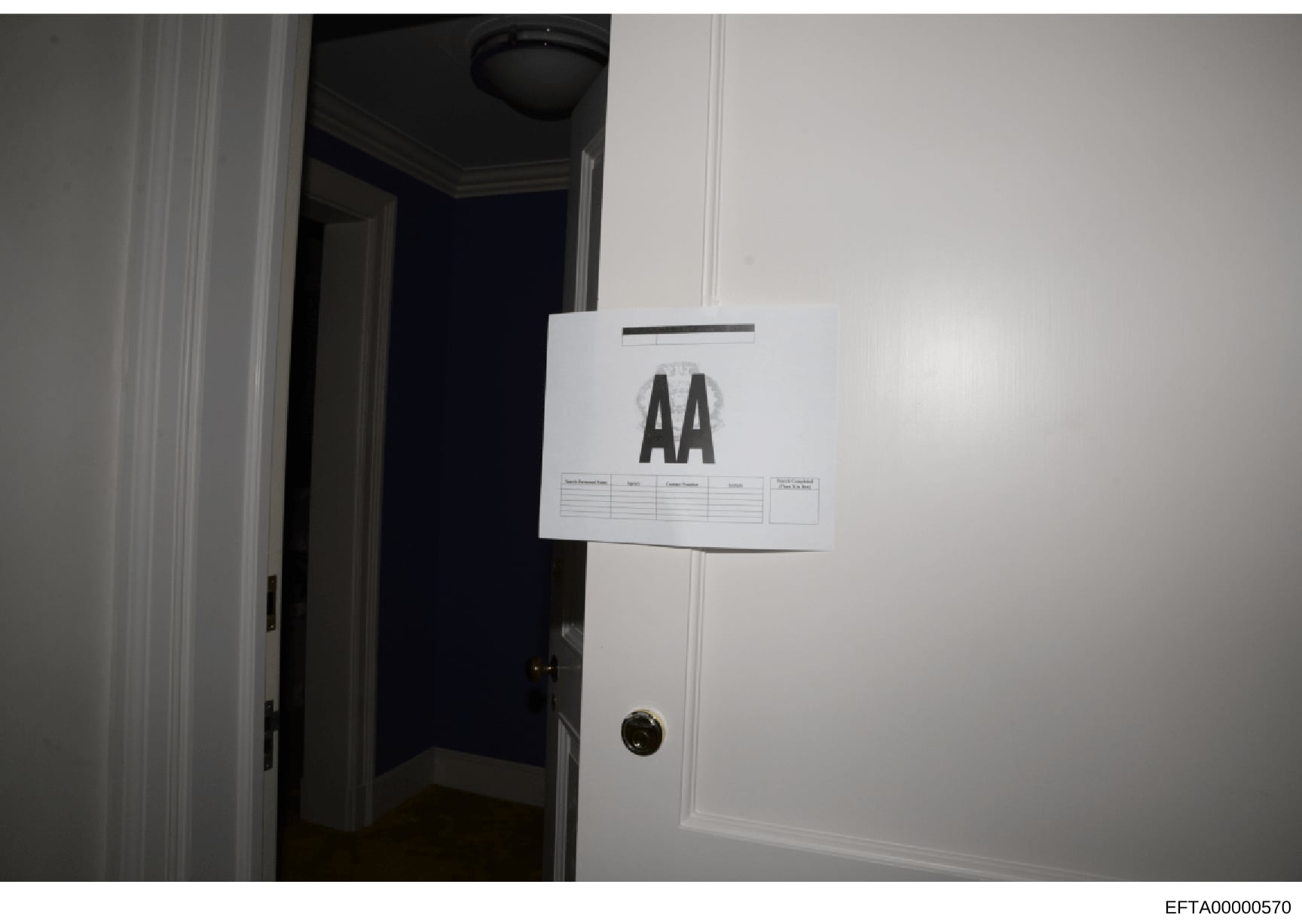 This is an evidence photograph showing an interior doorway with a white evidence marker labeled 'AA' attached to the door frame. The photo documents a room entrance with white trim, ceiling fixture, and brass doorknob. This type of documentation is s