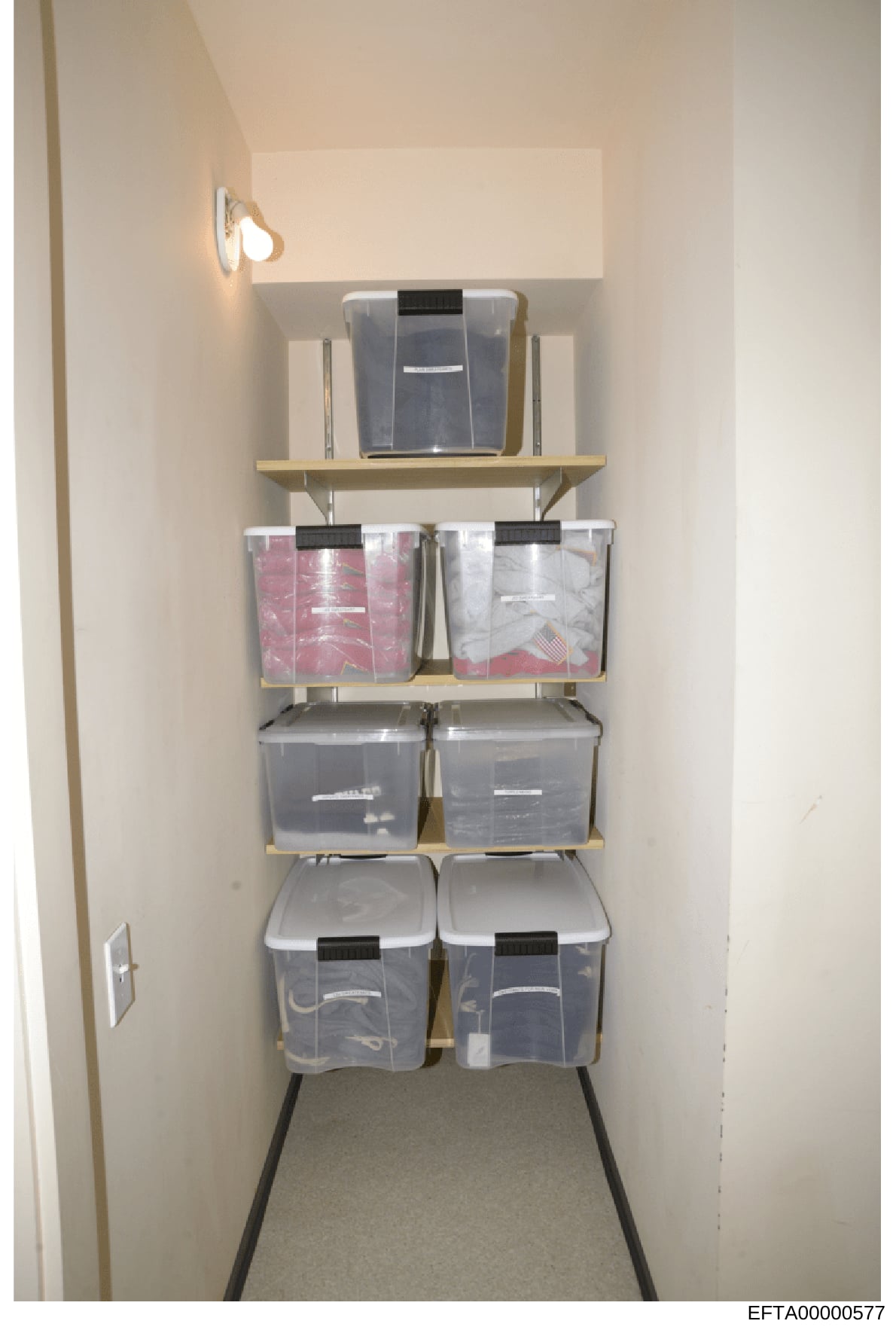 Evidence photograph showing an interior storage closet containing multiple clear plastic storage containers organized on wall-mounted shelving. The containers appear to hold various items including folded materials in pink and white packaging. This p