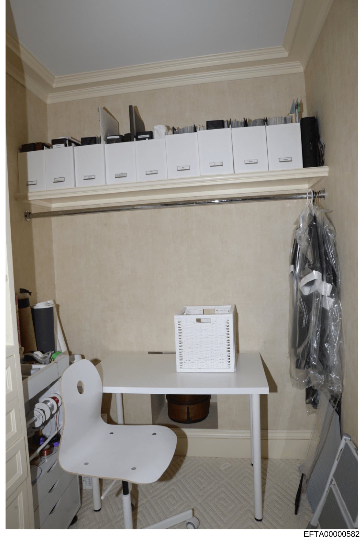 This photograph shows an organized office or administrative workspace featuring a shelving system with multiple white storage boxes, a simple desk setup with a white chair, and various organizational materials. The space appears to be part of a large