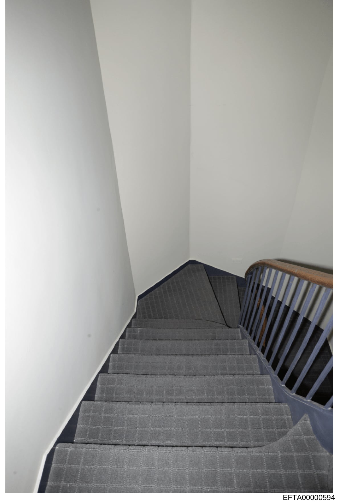This photograph shows an interior staircase viewed from above, featuring gray carpeted steps and a wooden handrail with blue-striped spindles. The stairs appear to be in a residential or commercial property. The image is taken from a downward angle,