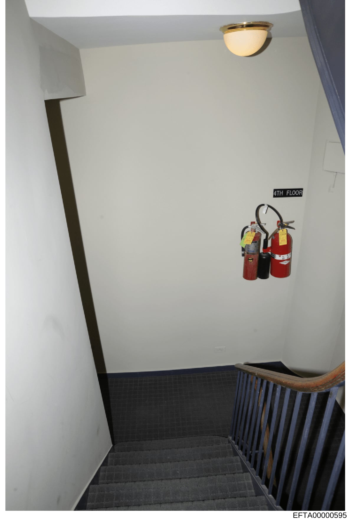 This is an evidence photograph of a stairwell on the 4th floor of a property, showing basic interior features including fire extinguishers mounted on the wall, ceiling fixtures, and building infrastructure. The photo appears to be part of a property 