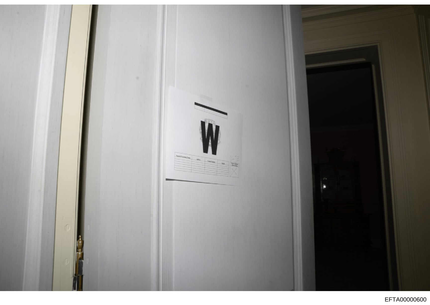 This is an evidence photograph from a property search or investigation showing an interior wall with an evidence marker labeled 'W' and what appears to be a small evidence documentation label or grid below it. The marking and documentation protocol s
