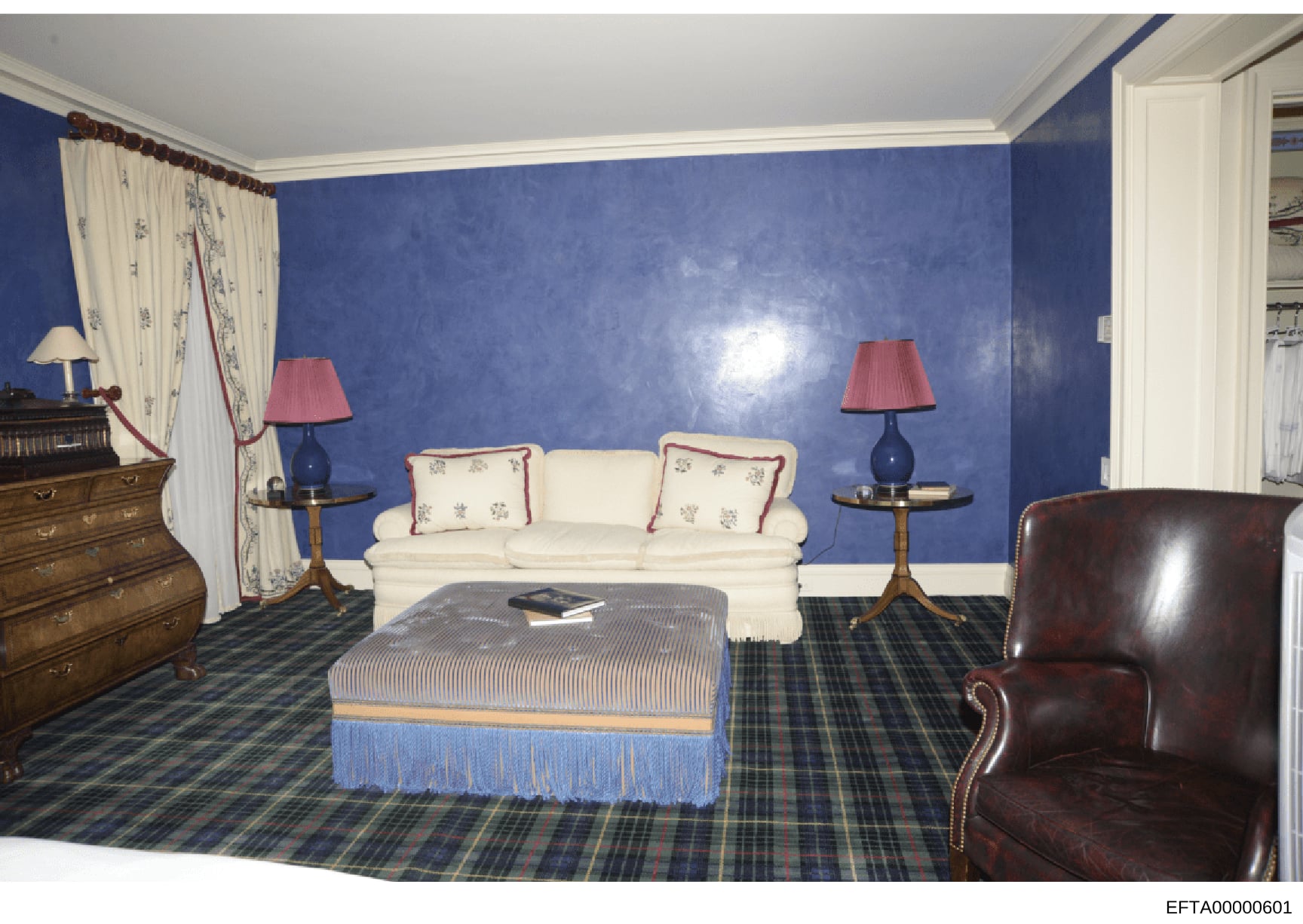 This is a photograph of an elegantly decorated interior room featuring blue walls, a cream-colored sofa, mahogany furniture, and formal décor. The image appears to be evidence documentation from the investigation, likely depicting one of Jeffrey Epst