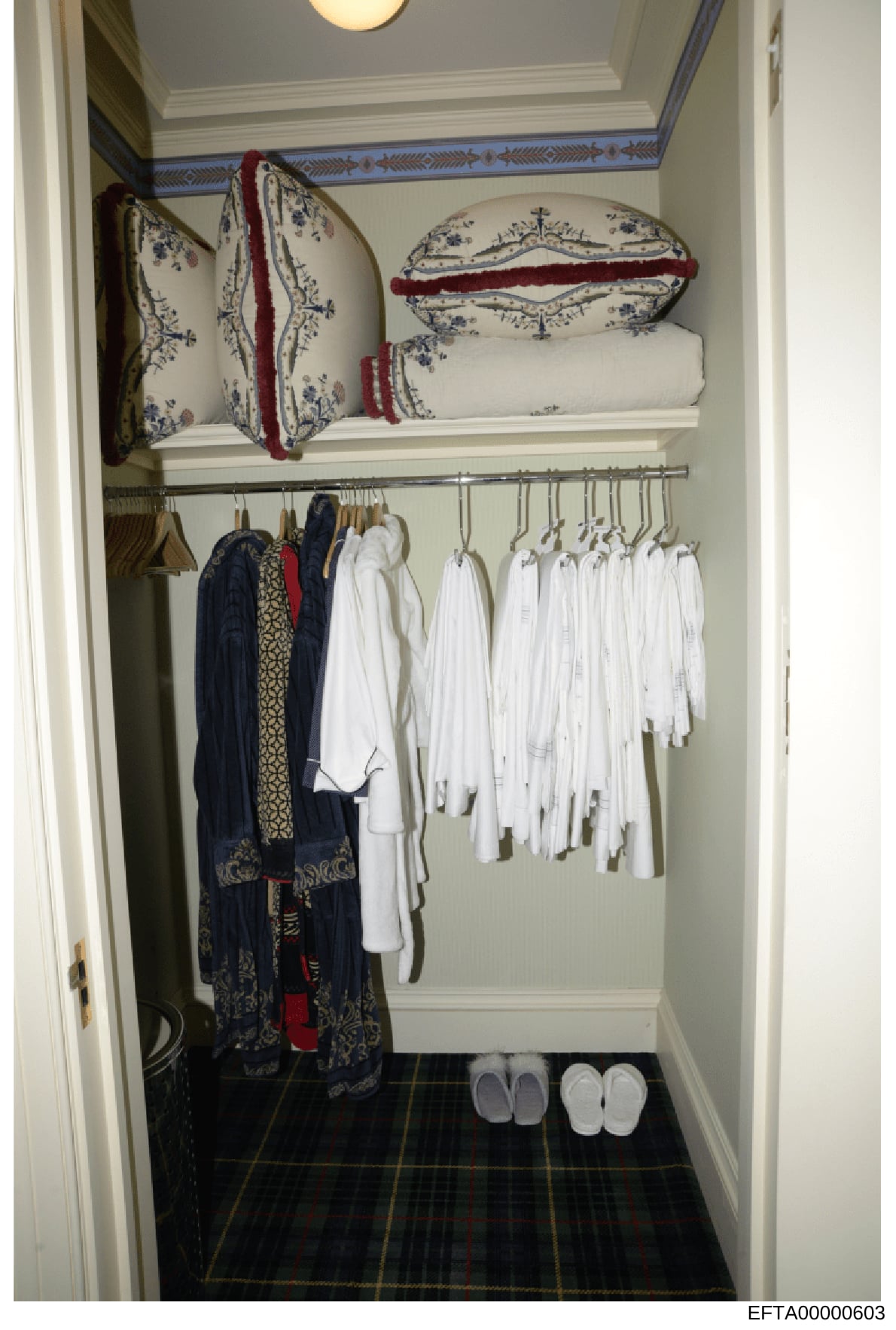 This is a photograph of an organized walk-in closet or linen storage area, likely from one of Jeffrey Epstein's properties. The closet contains decorative pillows with burgundy trim, stacks of white linens, hanging white garments, ornate robes or caf