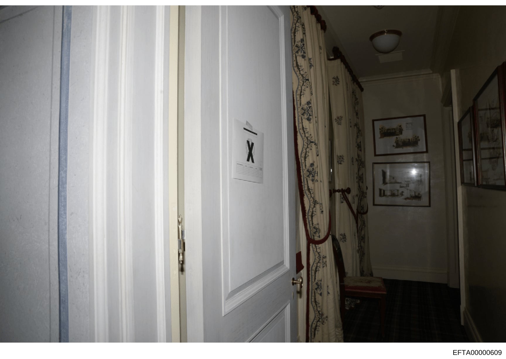 This is an evidence photograph showing an interior hallway of a property, featuring a white door marked with an 'X' and what appears to be evidence documentation. The image captures the hallway's architectural details including decorative wallpaper,