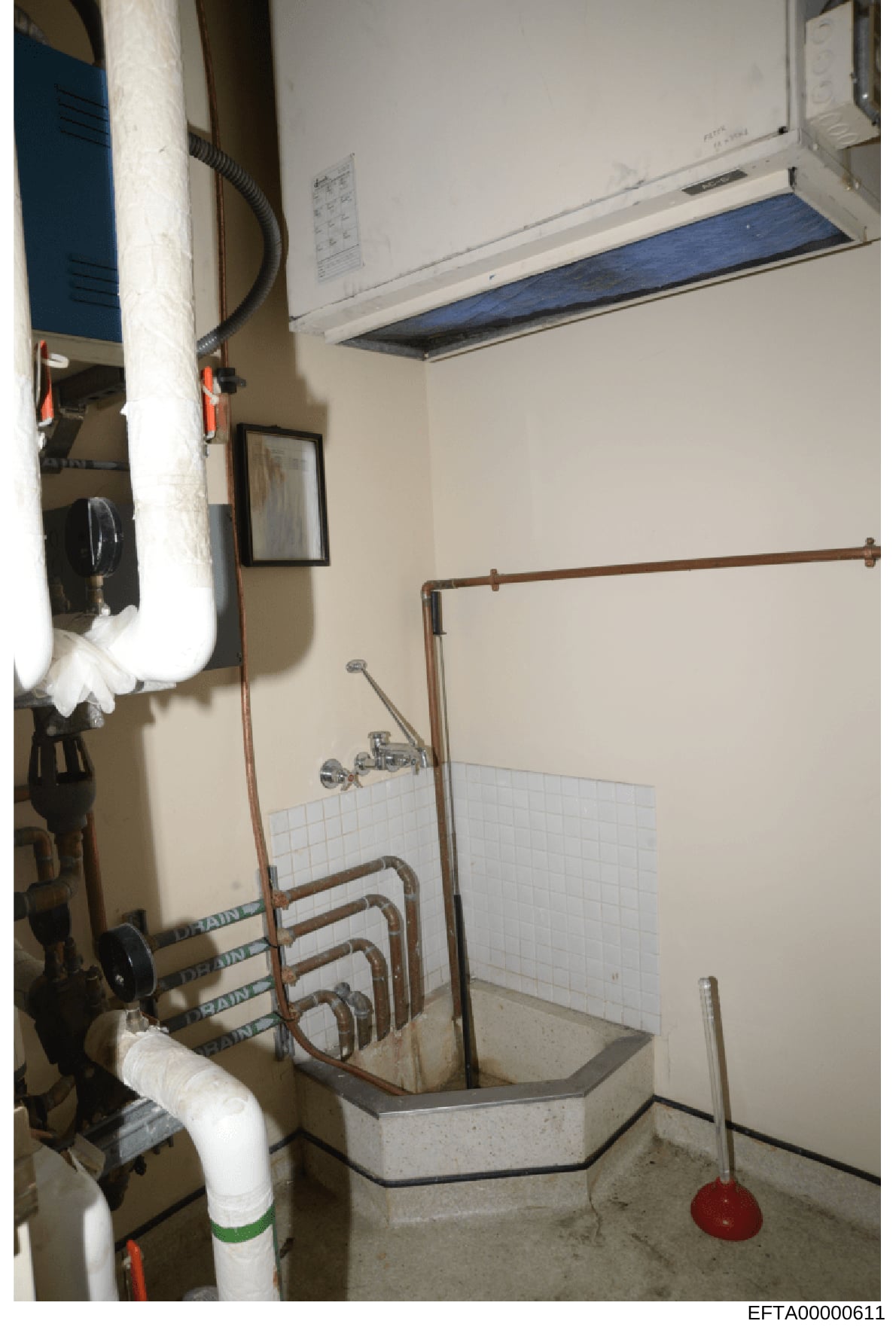 This photograph shows an interior utility/bathroom space containing HVAC equipment, plumbing infrastructure, and heating systems. The image appears to be evidence documentation from a property inspection, likely taken during the investigation of one 