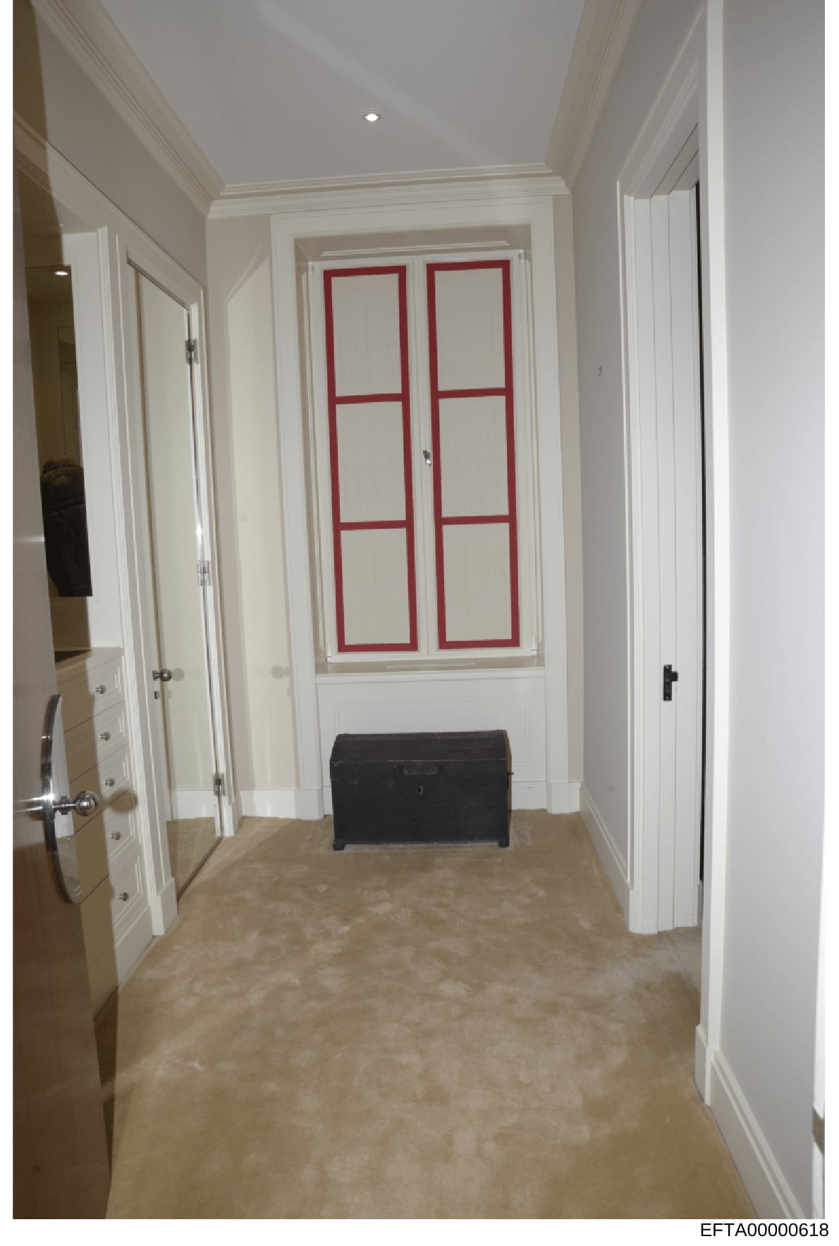 This is an evidence photograph depicting an interior hallway of a residential property, featuring white painted walls, recessed ceiling lighting, multiple white panel doors on either side, and a distinctive white door with red geometric frame pattern