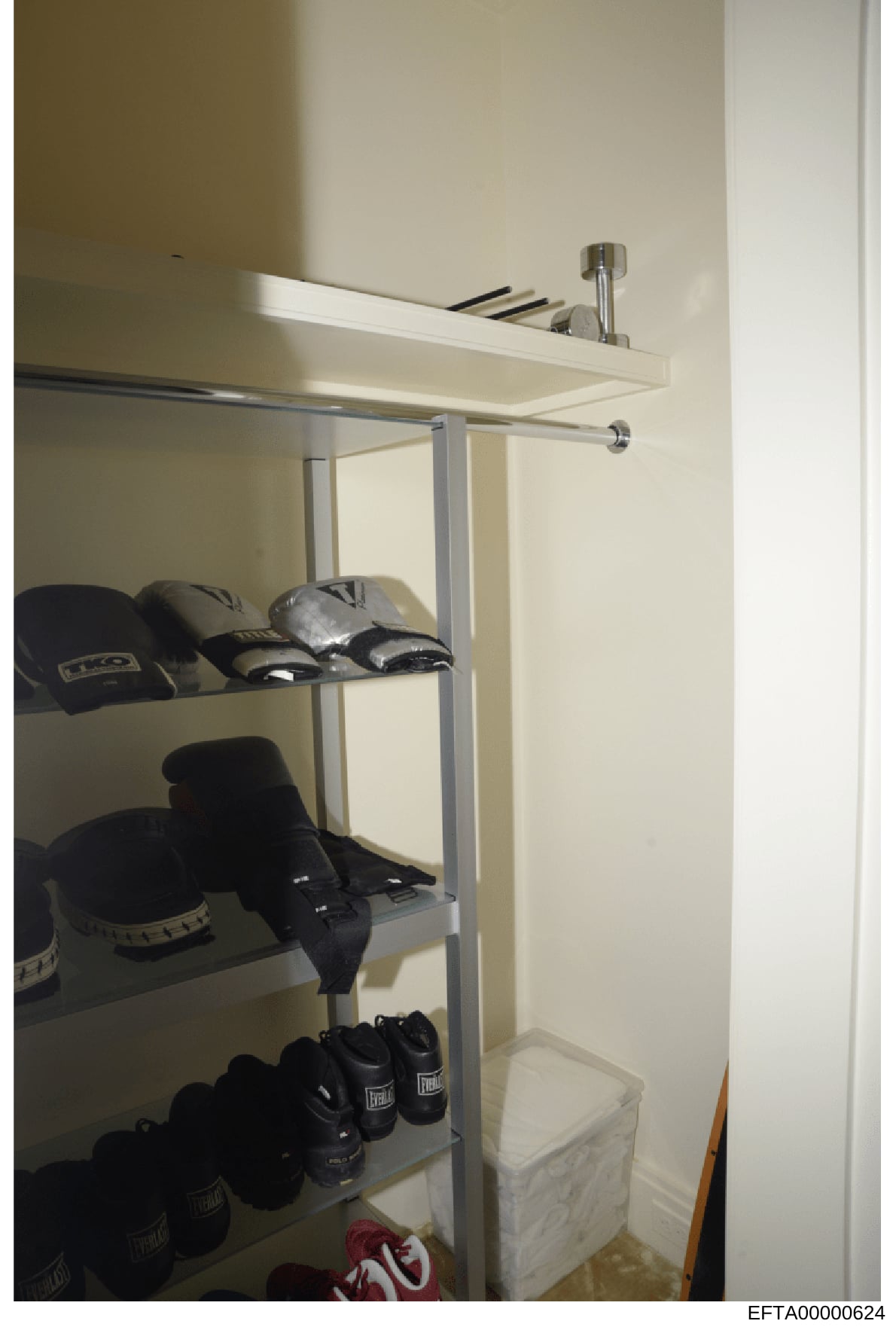 This is a photograph of a closet or storage room containing athletic equipment, primarily boxing gloves and hand wraps. The shelving unit displays multiple pairs of black boxing gloves branded 'Everlast' across three shelves, along with hand wraps an