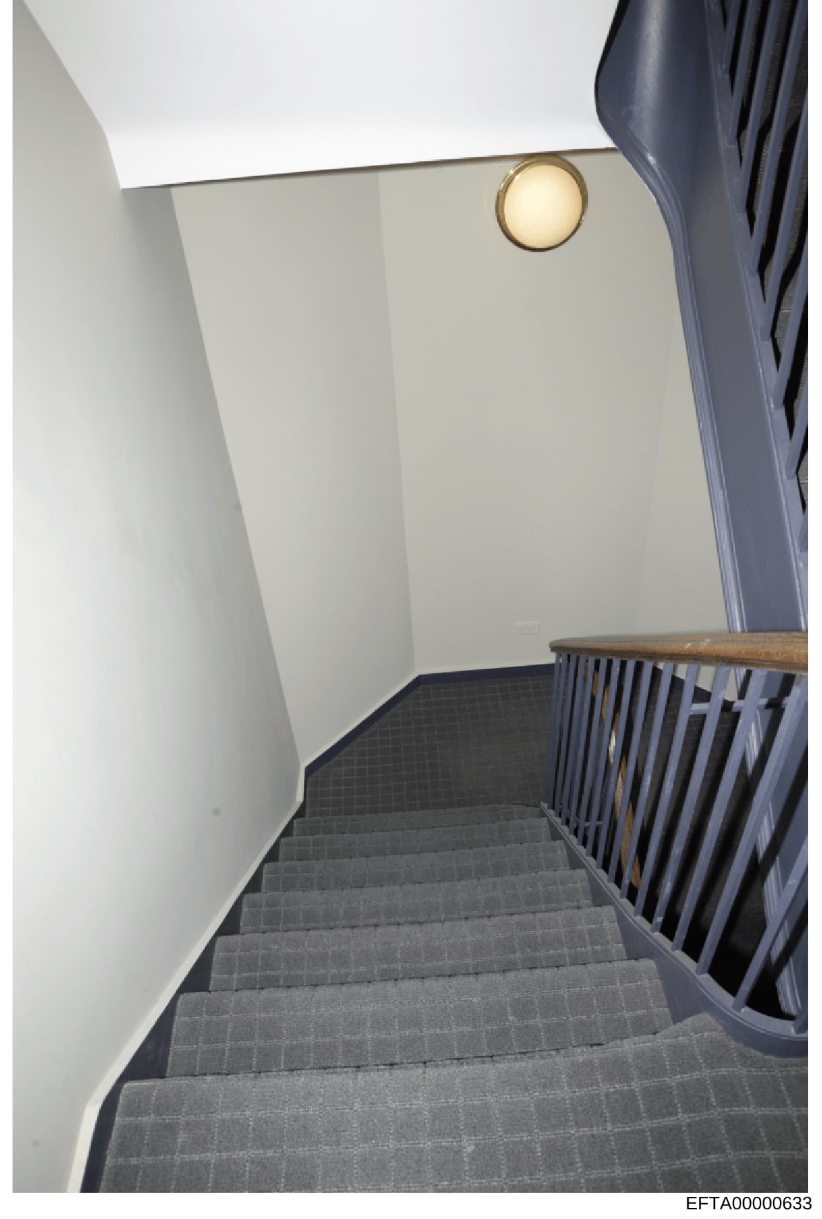 This is a photograph of an interior stairwell, showing a modern residential space with white walls, gray carpeted stairs, a wooden handrail, and brass wall sconce lighting. The image appears to be evidence documentation of property interior, likely f